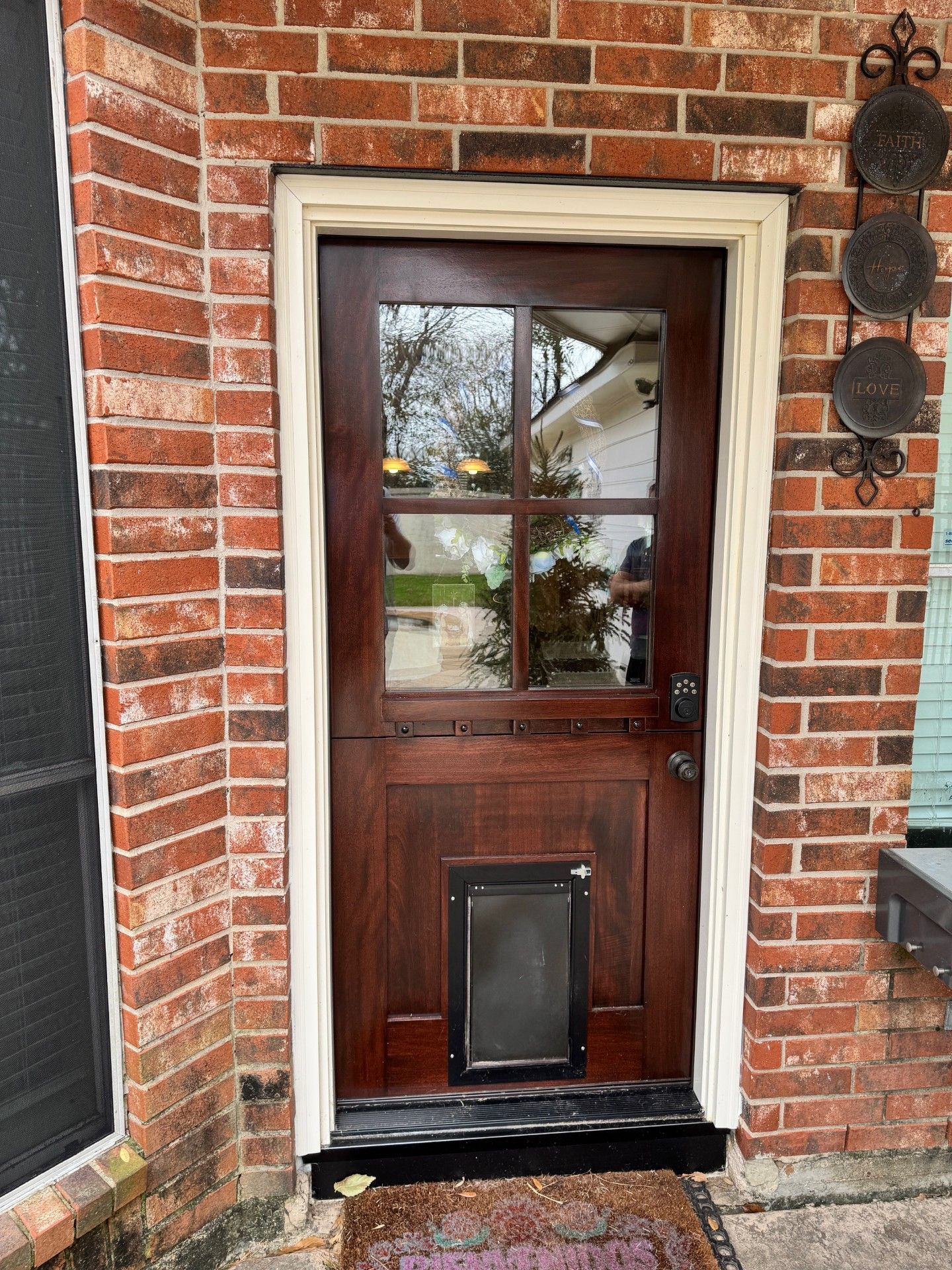 Dark wooden front door with glass panes in a red brick wall beside a window and porch light