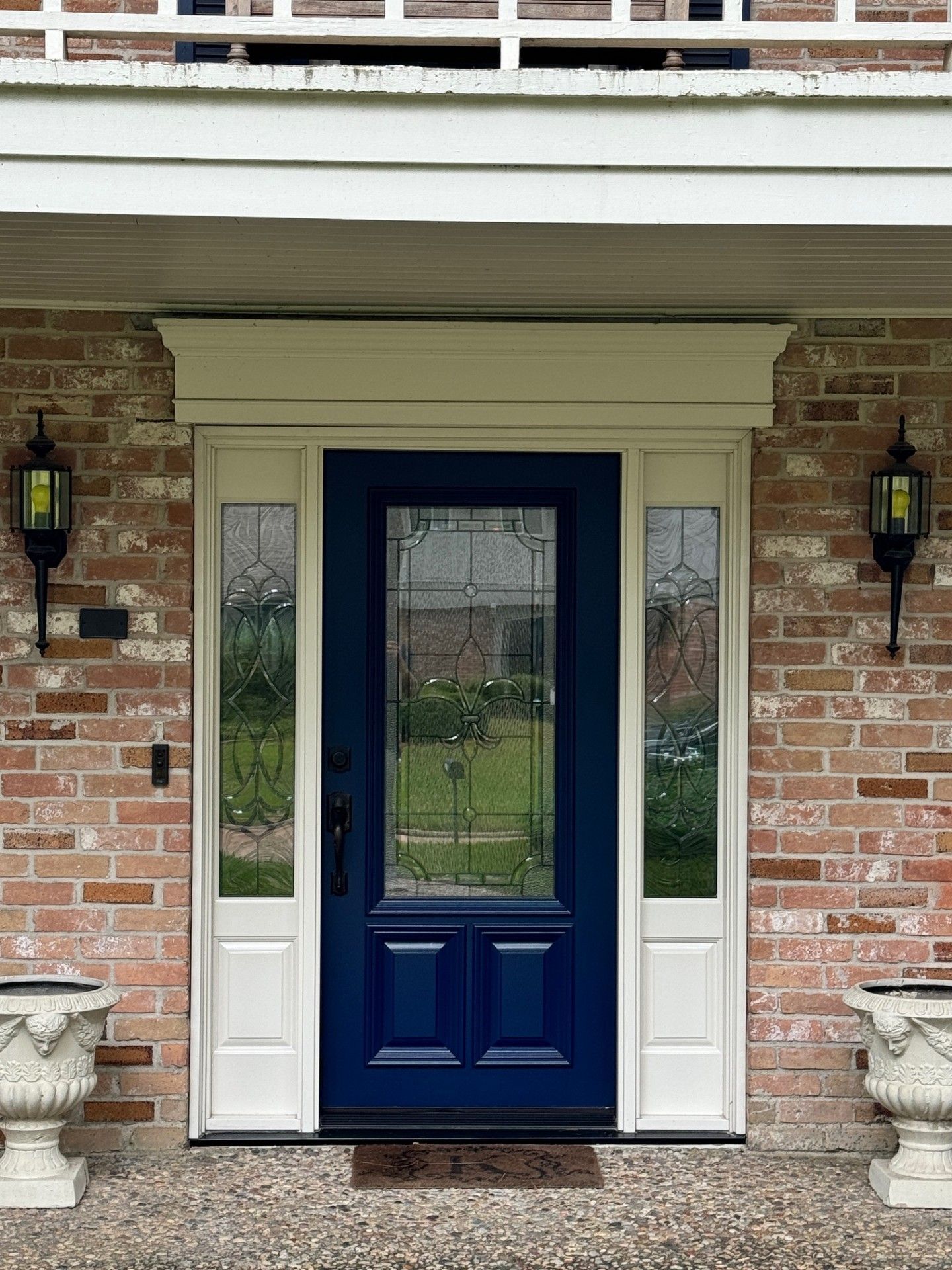Front entry with a navy door, sidelights, and brick exterior flanked by wall lanterns.