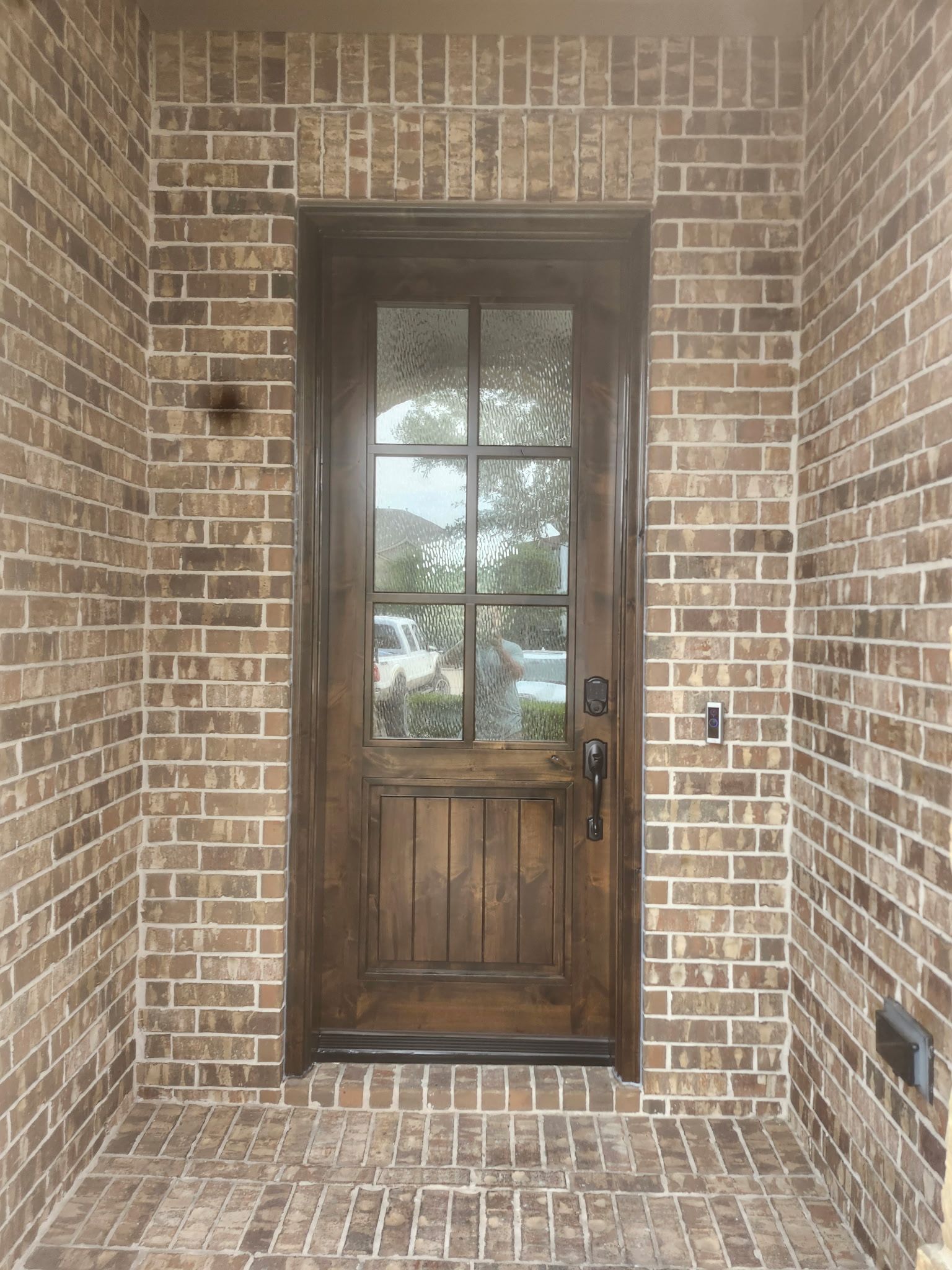 Brick front porch with a wooden glass-paneled door centered in the entryway