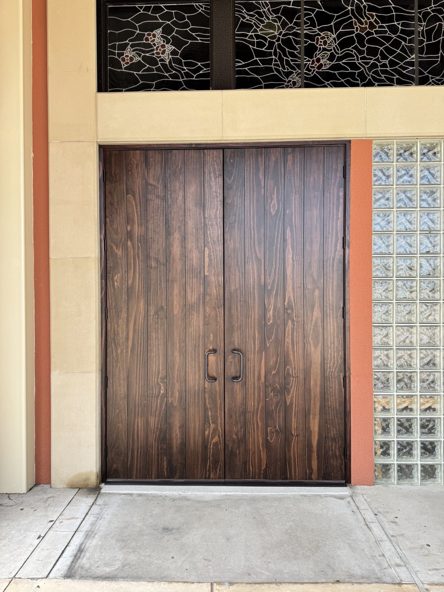 Wooden double doors set in a beige exterior wall beside glass block windows.