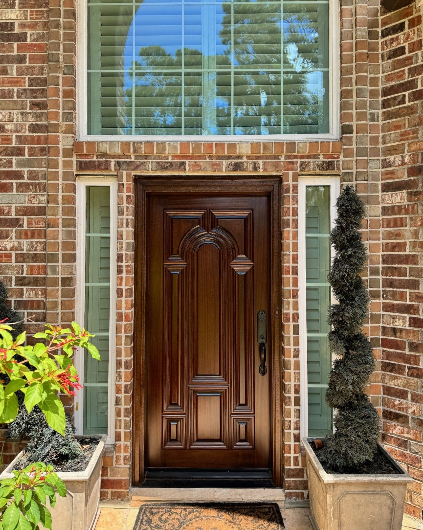 Brick entryway with a carved wooden front door, flanked by planters and a window above.