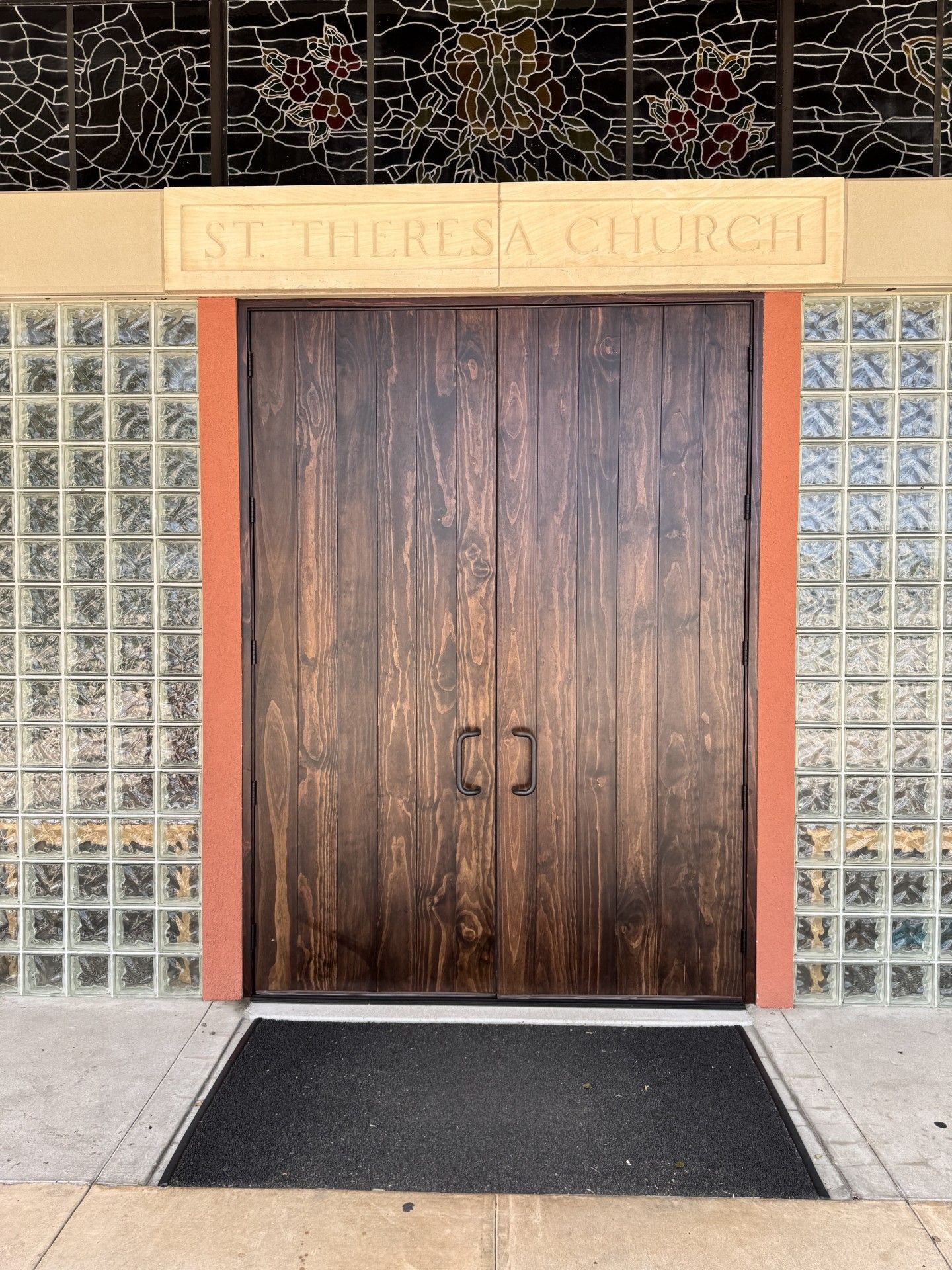 Wooden church entrance with glass block side walls and a tan “St. Theresa’s Church” sign above.