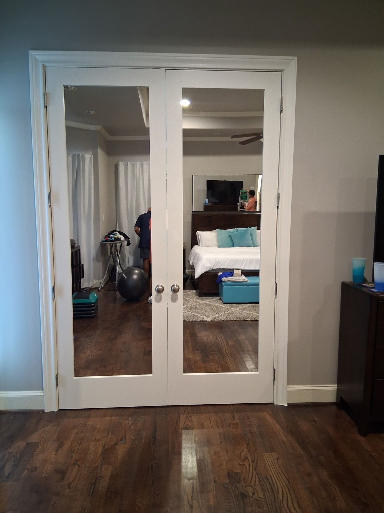 White double doors with mirrors in a bedroom, showing a bed, TV, and exercise bike inside.