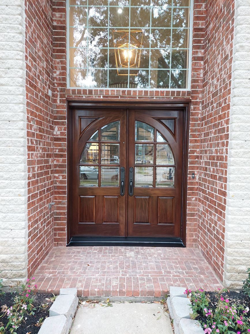 Brick entryway with dark wood double front doors and a large window above