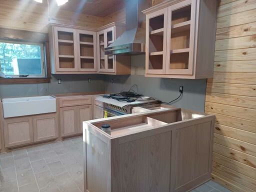 Modern kitchen with light wood cabinets, tiled floor, central island, and large window.