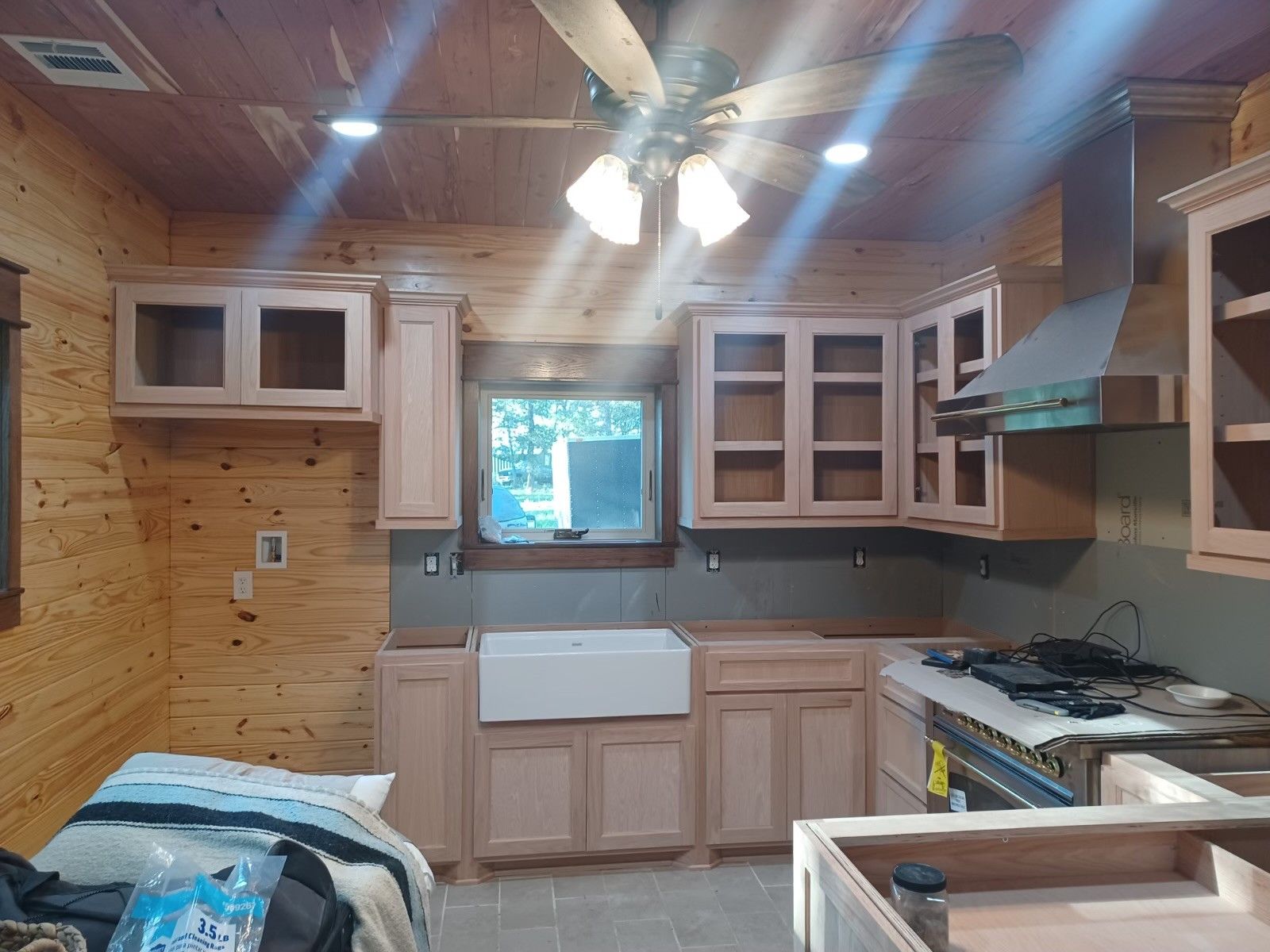 Small rustic kitchen with wood paneling, white cabinets, a farmhouse sink, and a gas stove.