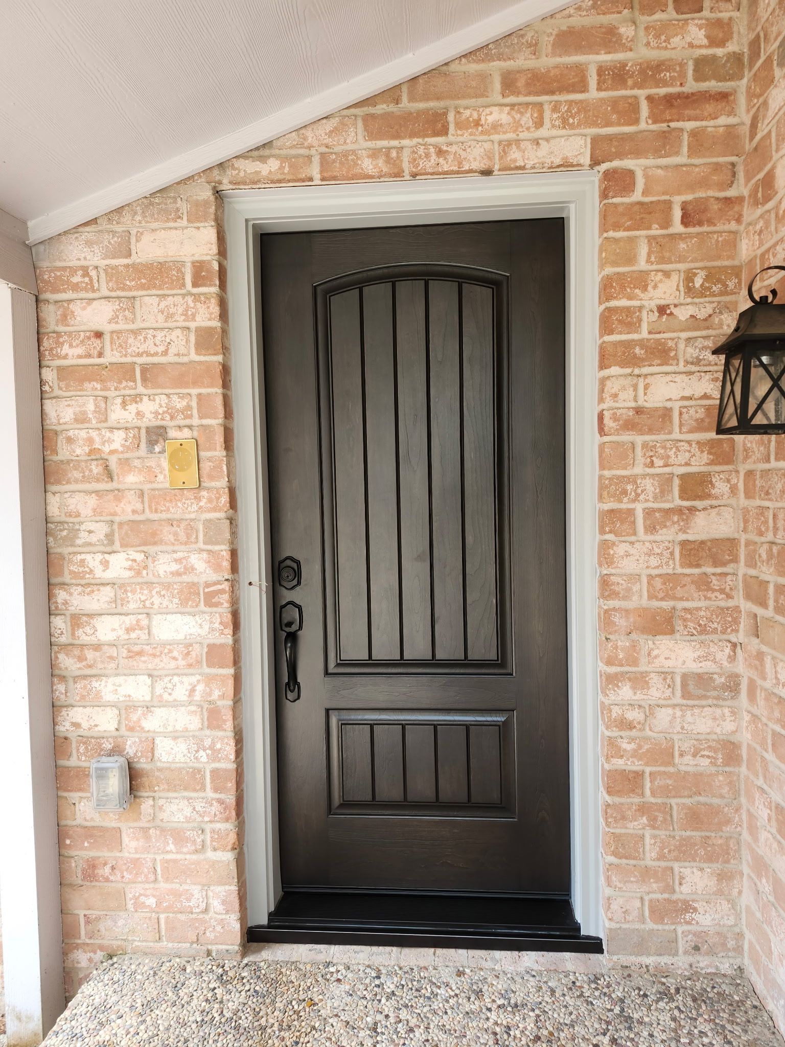 Black front door set in a brick porch with a tiled threshold and wall lanterns