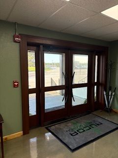 Glass double doors in a lobby with a welcome mat and coat rack, viewed from inside.