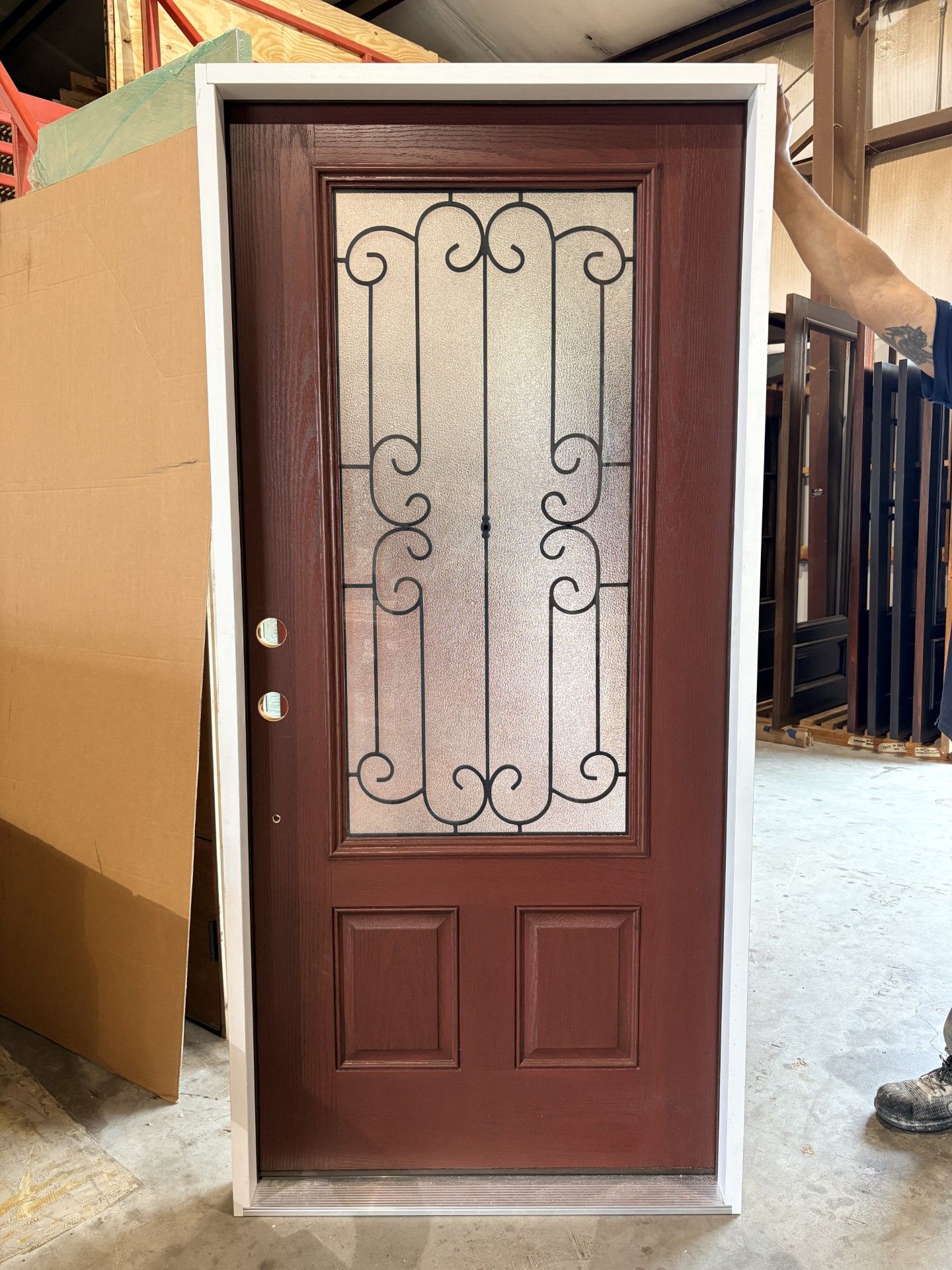 Brown wooden door with decorative glass panel and black wrought-iron scrollwork, standing outdoors.
