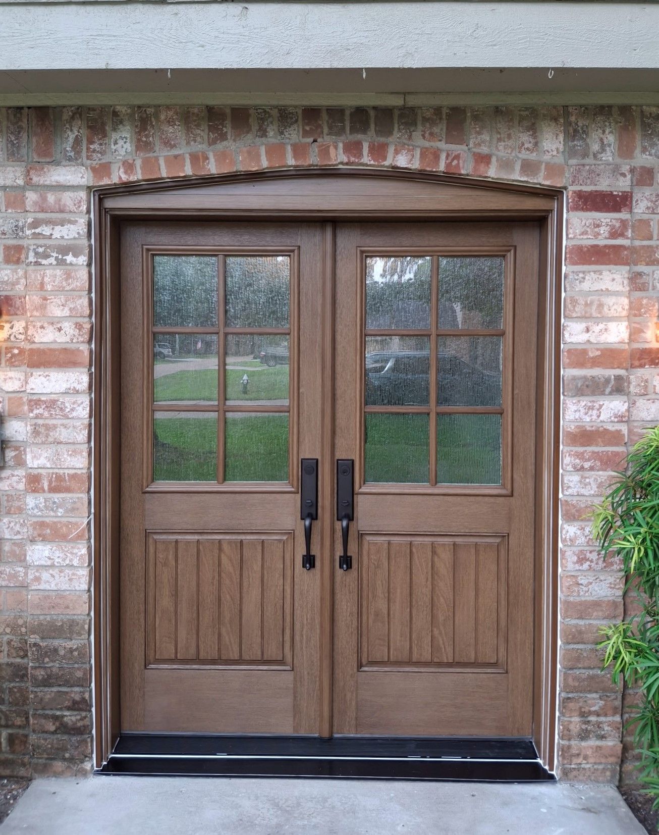 Wooden double front doors with glass panes set in a red brick exterior wall.