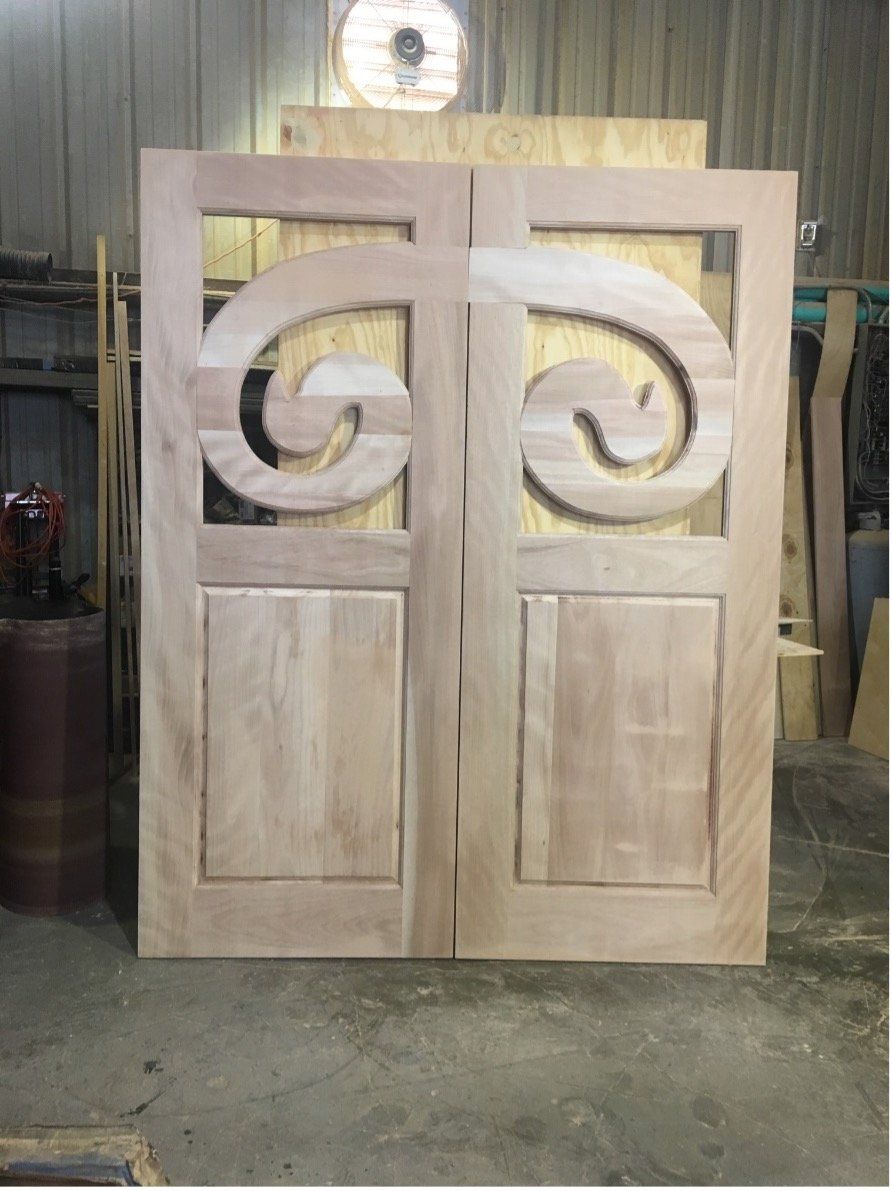 Unfinished wooden double doors with decorative swirl panels in a workshop