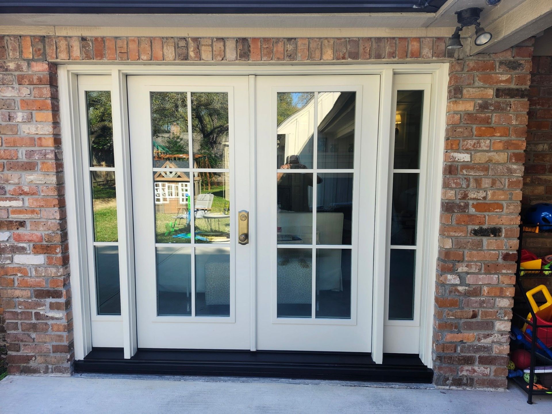 White front entry with double glass doors, brick walls, and narrow sidelights under a covered porch.