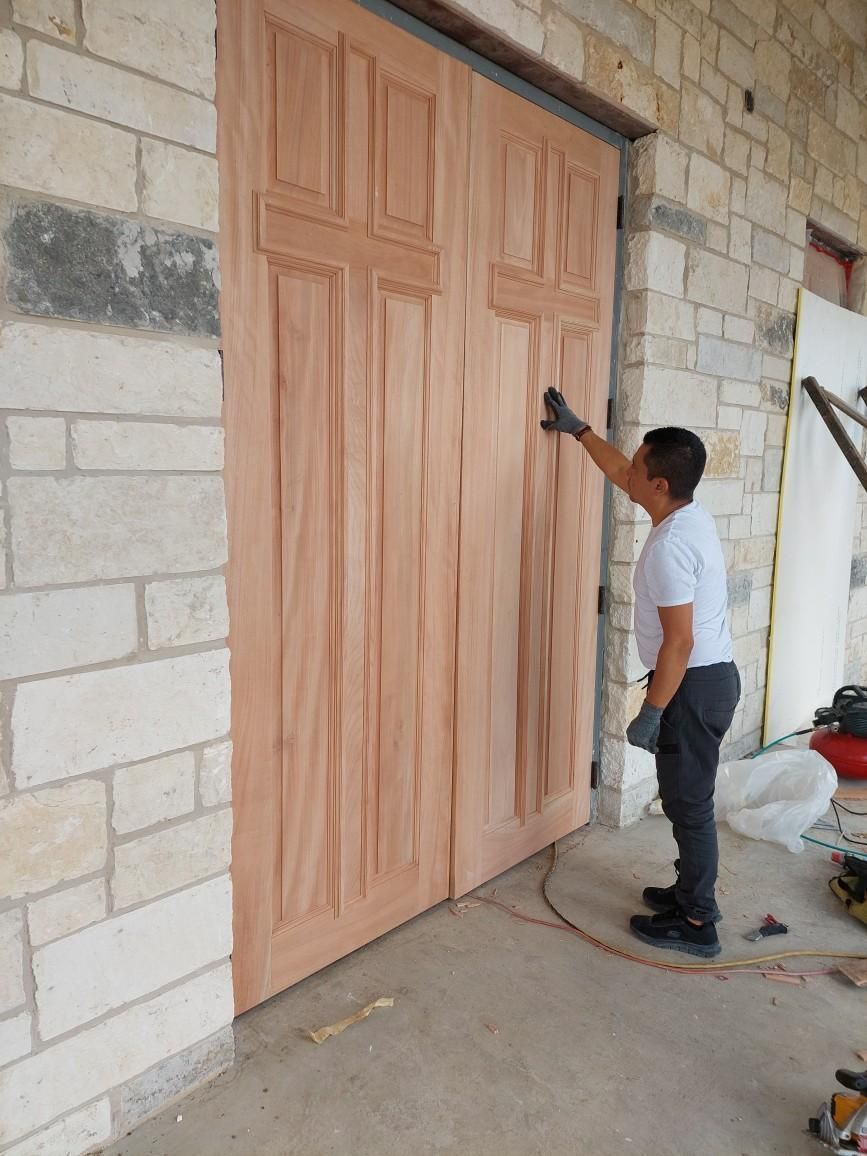 Man standing beside a large wooden door, reaching up toward the top latch on a stone wall.