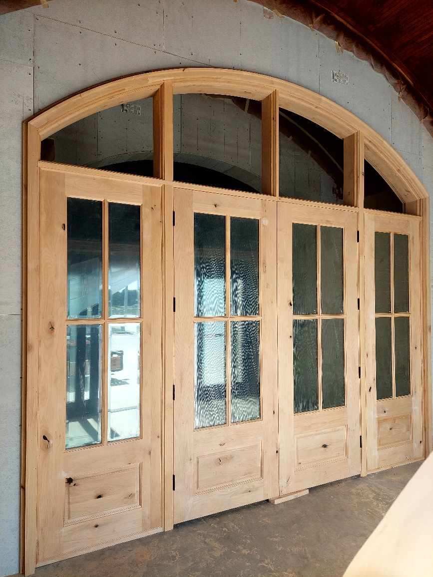 Wooden arched double doors with glass panes set in a white stucco entryway