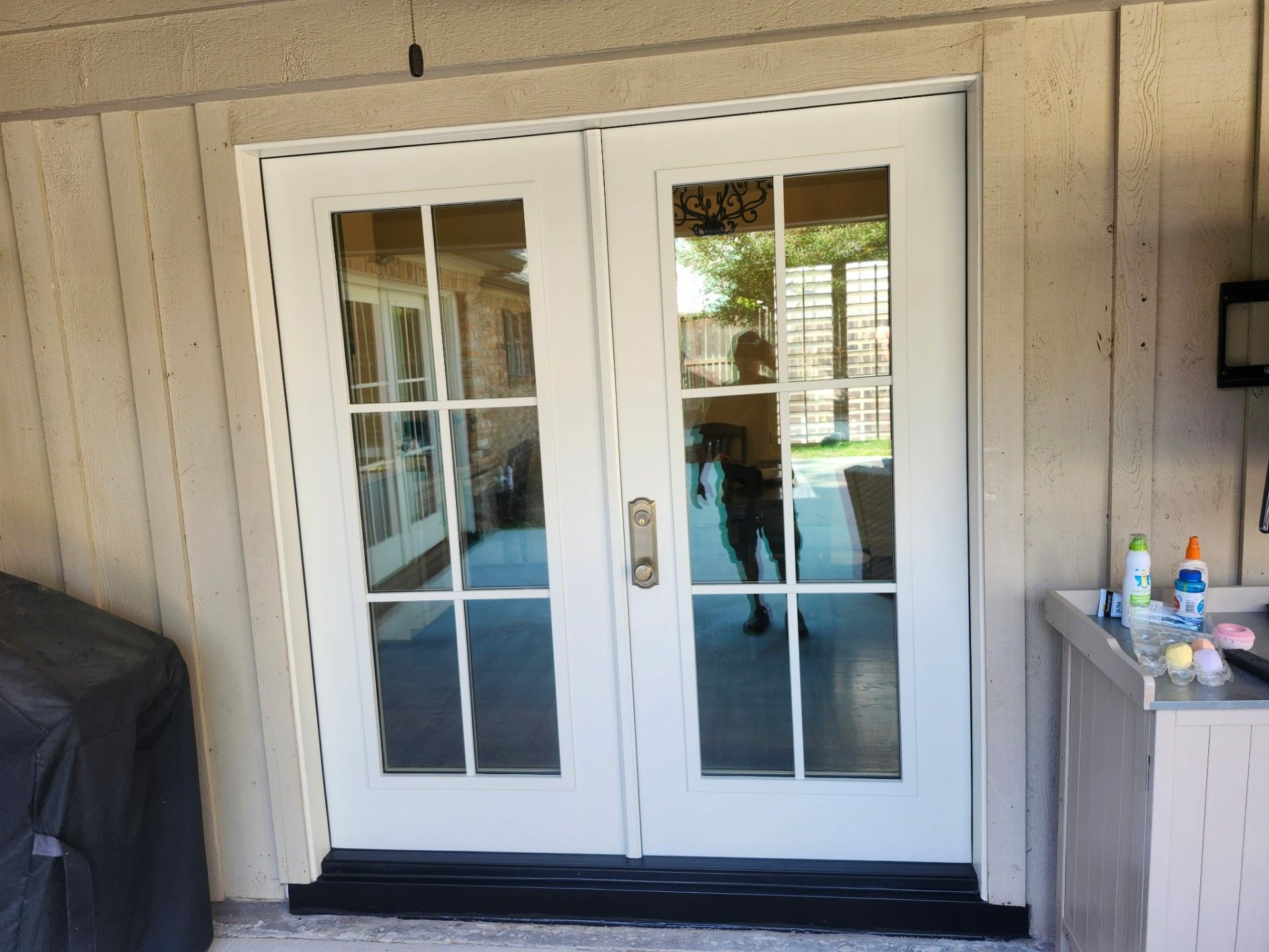 White French doors with glass panes and a black mat at a beige house entrance