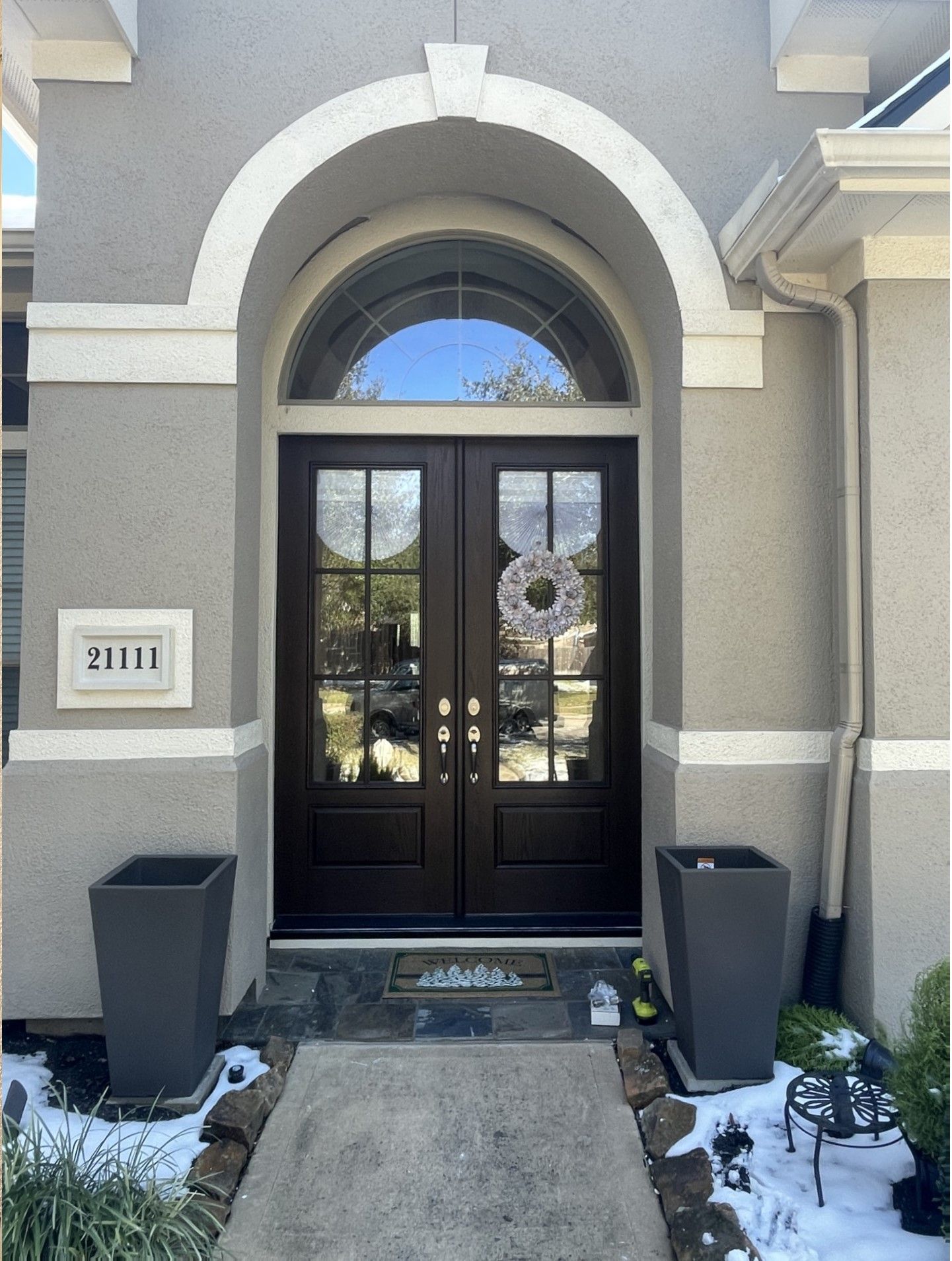 Front entrance with black double doors, arched frame, and two planters beside a concrete walkway.
