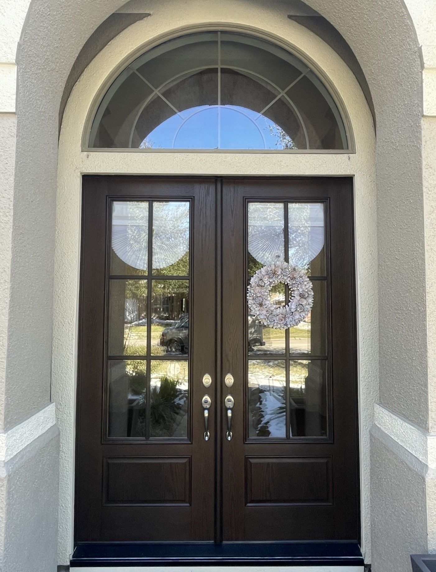 Dark double front doors with glass panels and arched window above on a stucco entryway