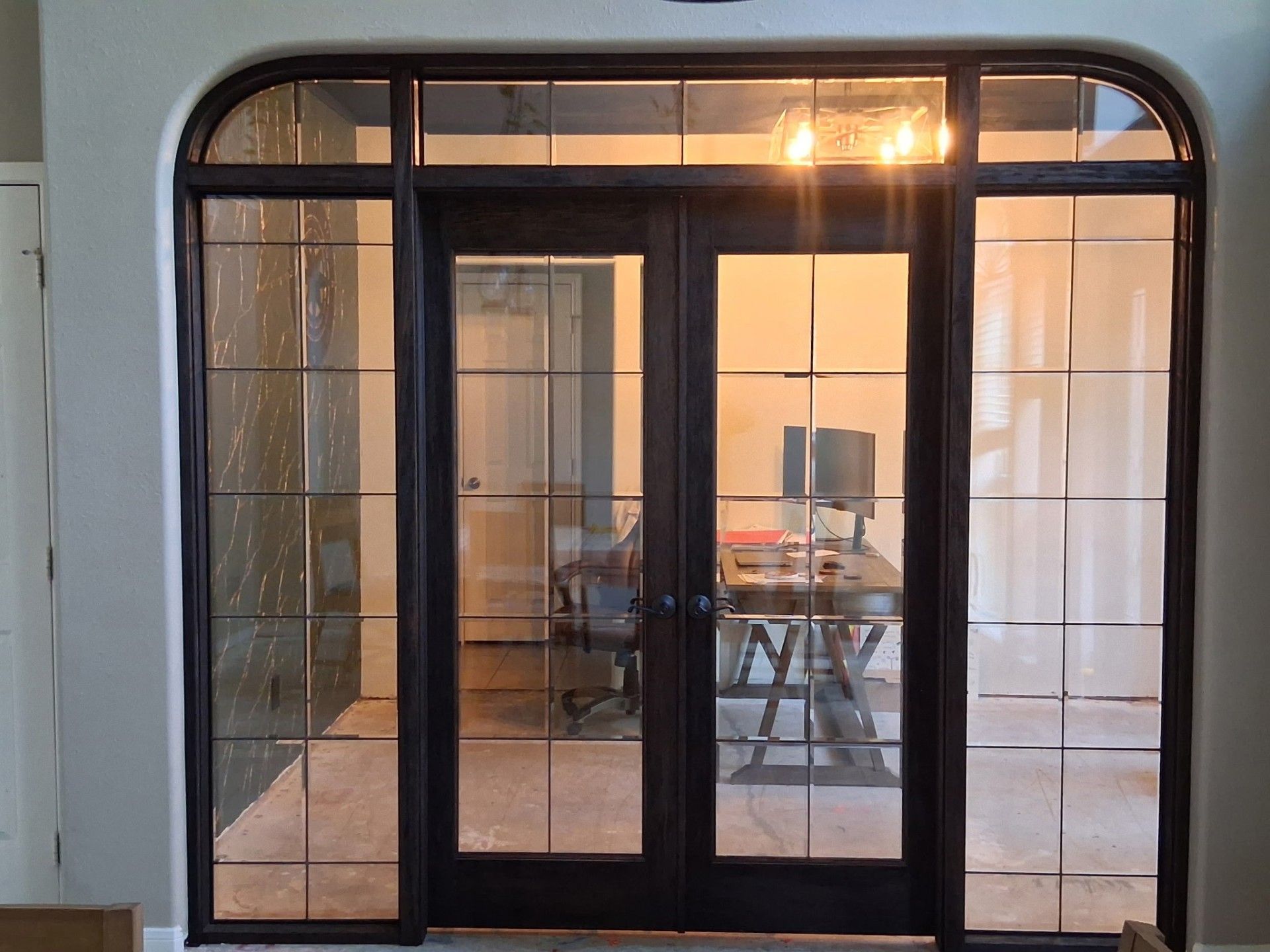 Black-framed glass double doors in an arched entryway, revealing a modern interior beyond.