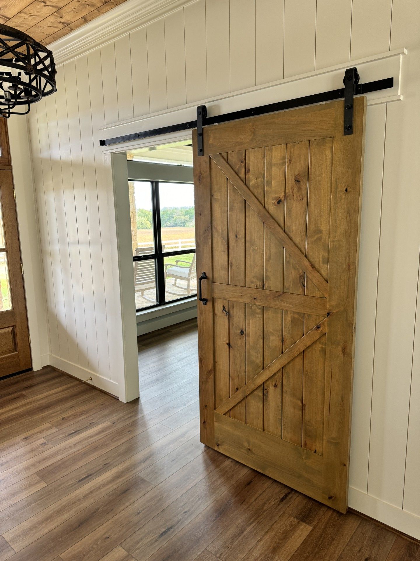 Rustic wooden barn door sliding on a track in a bright interior hallway with wood floors.