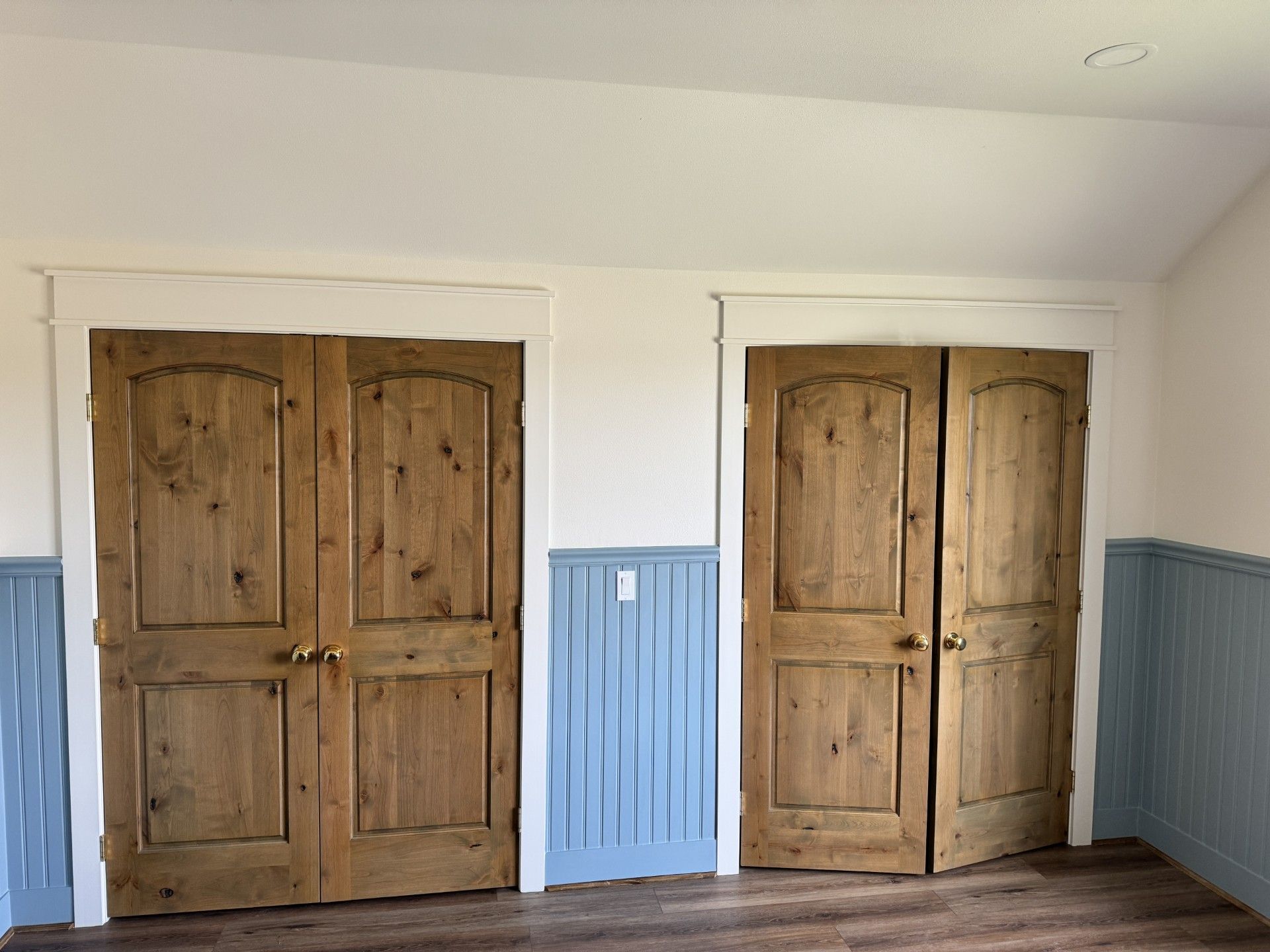 Two wooden double doors in a white hallway with blue wainscoting and trim