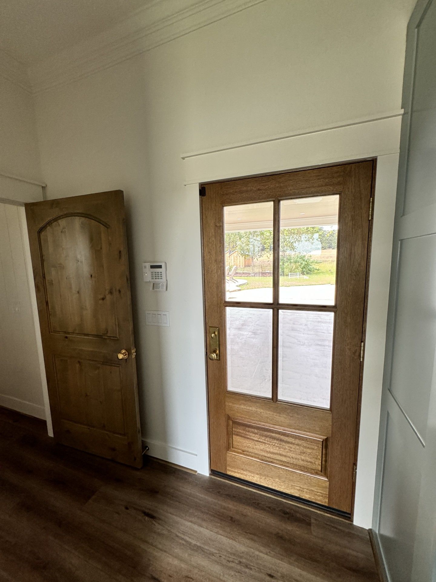 Wooden front door with glass panes beside a solid wood interior door in a bright hallway