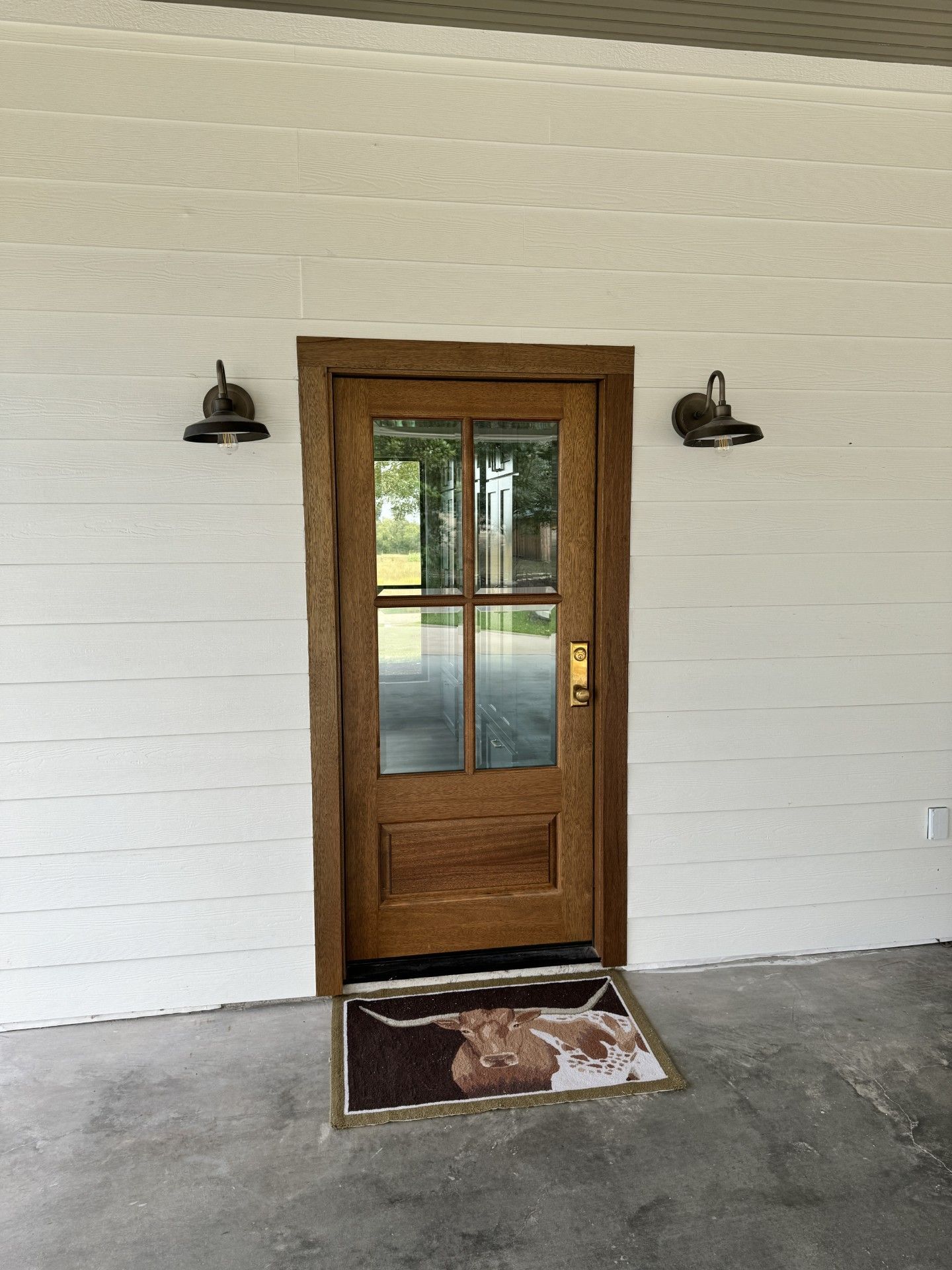 Wooden front door with glass panes between two black wall lamps on a white porch wall