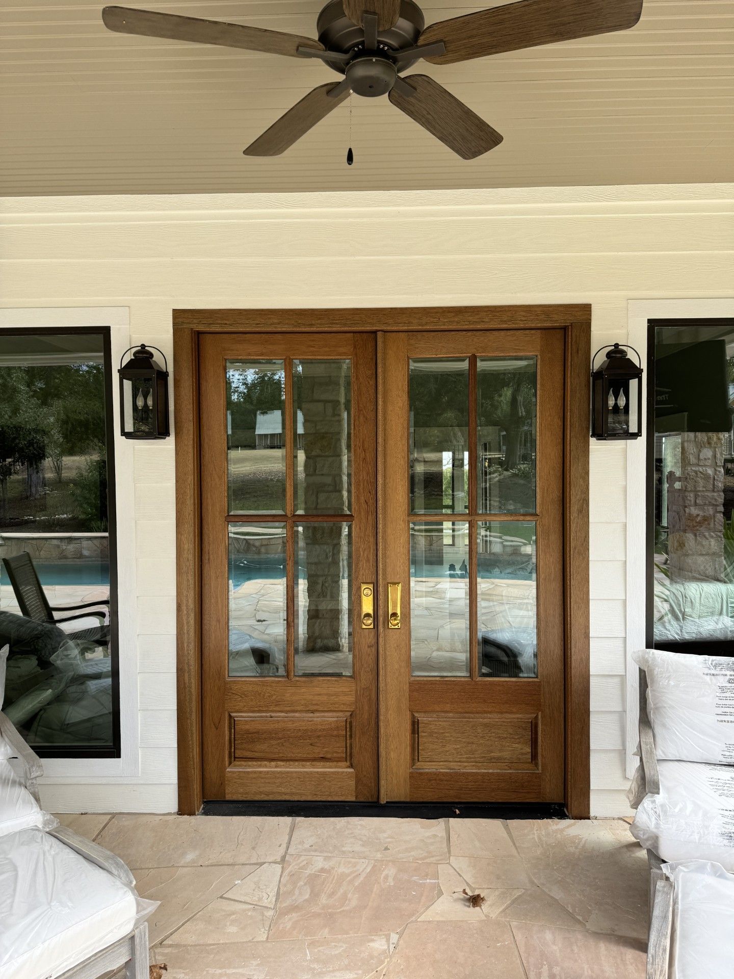 Wooden double French doors opening to a screened patio with ceiling fan and stone floor.