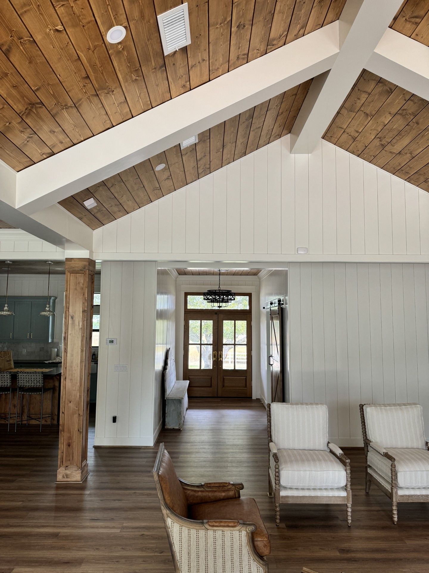 Bright living room with vaulted wood ceiling, white walls, and two white armchairs near a doorway.