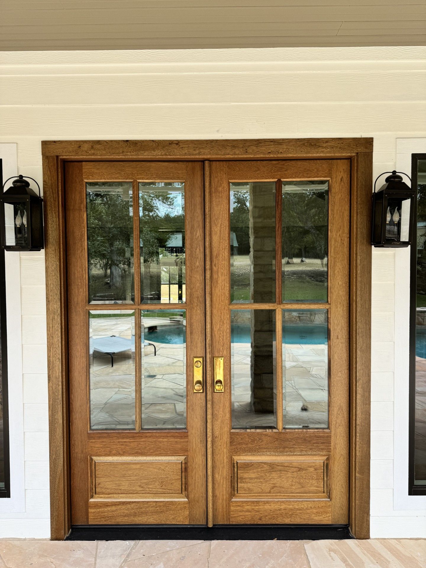 Wooden double front doors with glass panes and black wall lanterns on a cream exterior wall