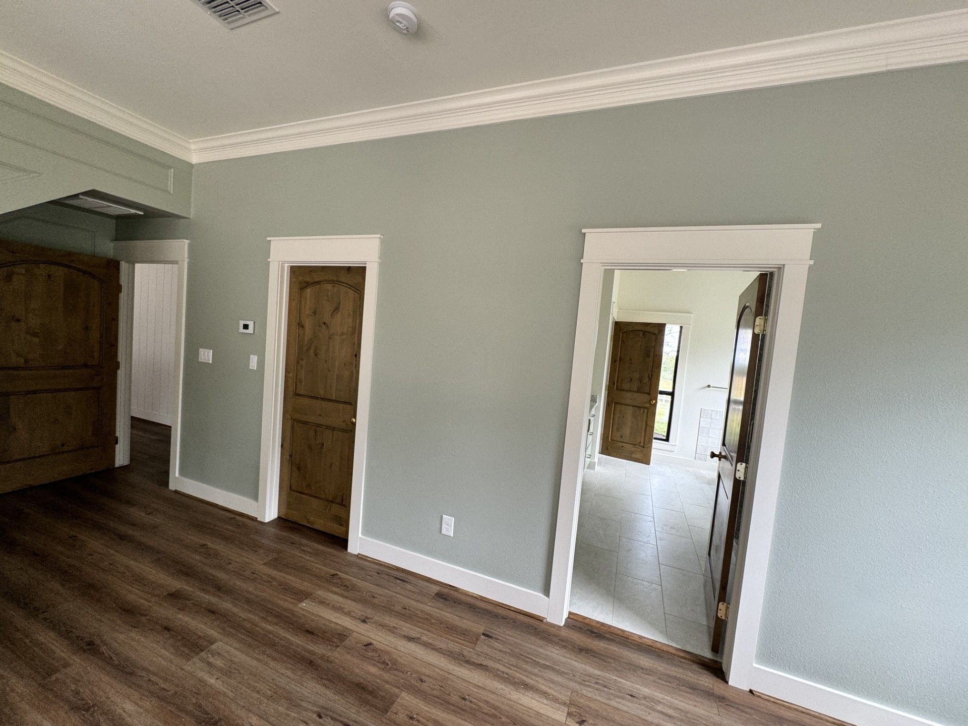 Empty room with gray walls, wood floors, and two open doorways leading to another room.