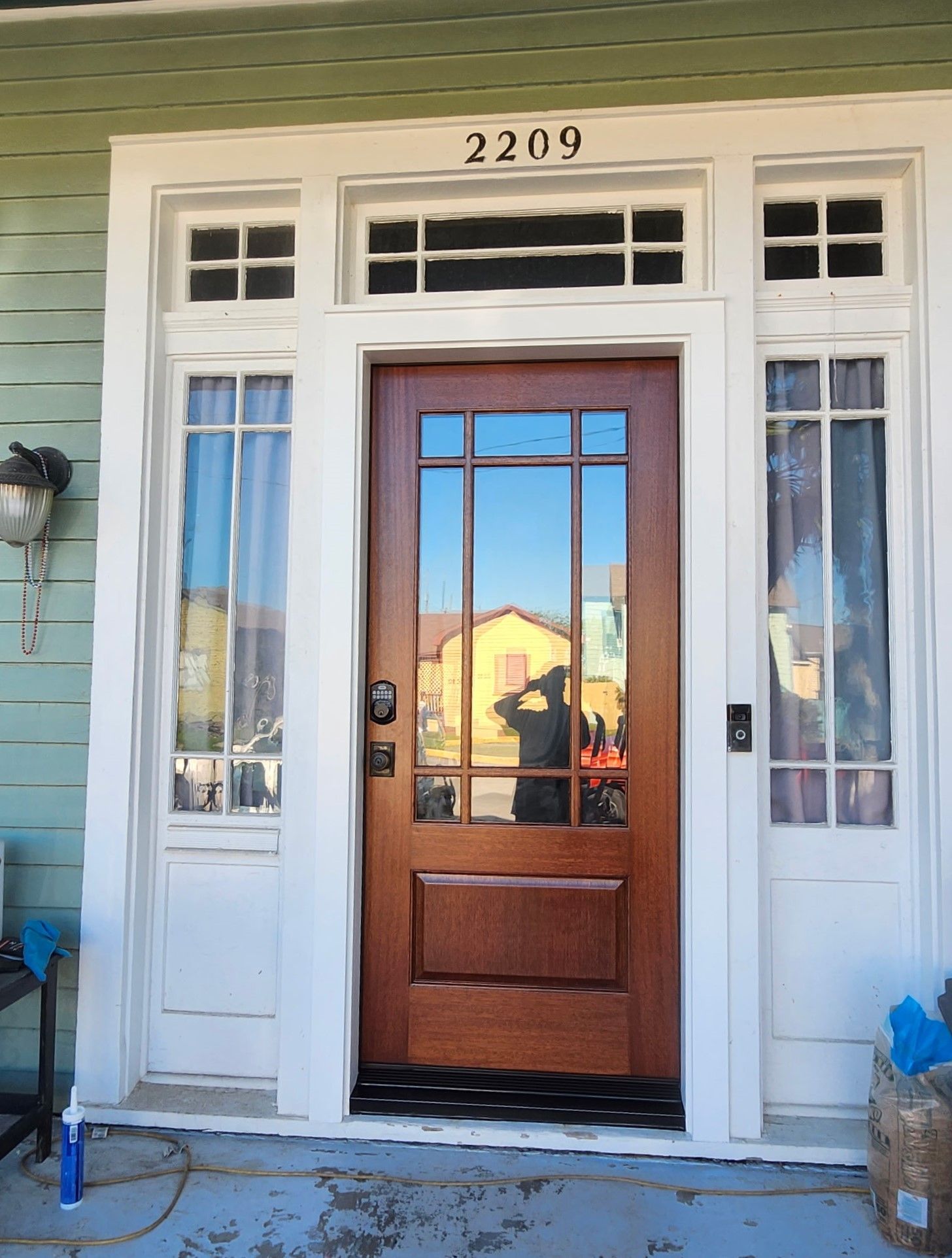 Front door with glass panels and house number 2209, framed by white trim and green siding.