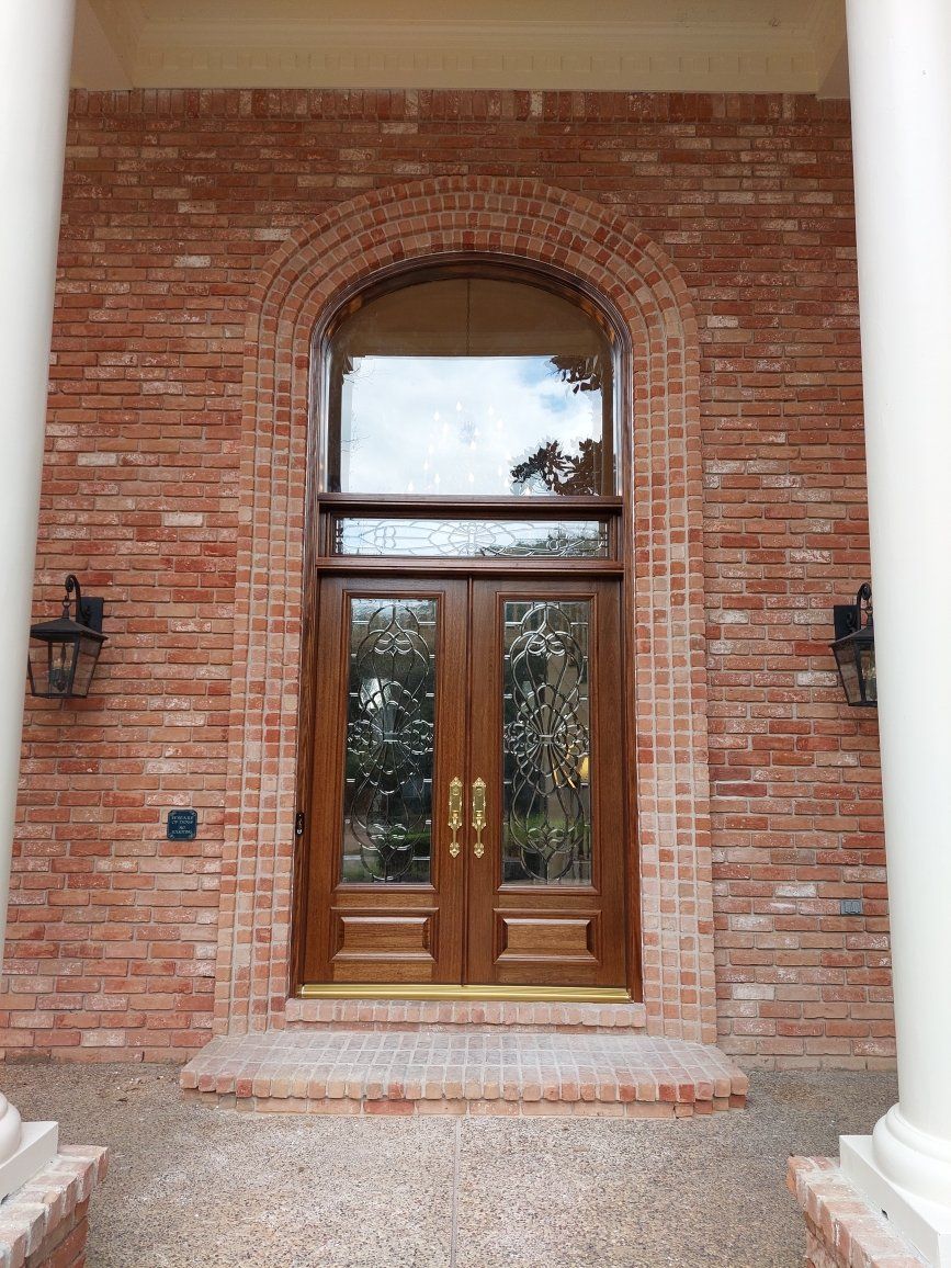Brick house entrance with arched wood-and-glass double doors and sidelights under a transom window