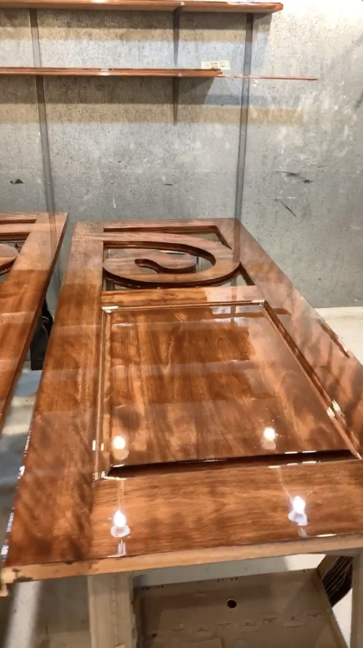 Wooden display table with glossy finish and a circular carved center, set against a gray wall with shelves above.