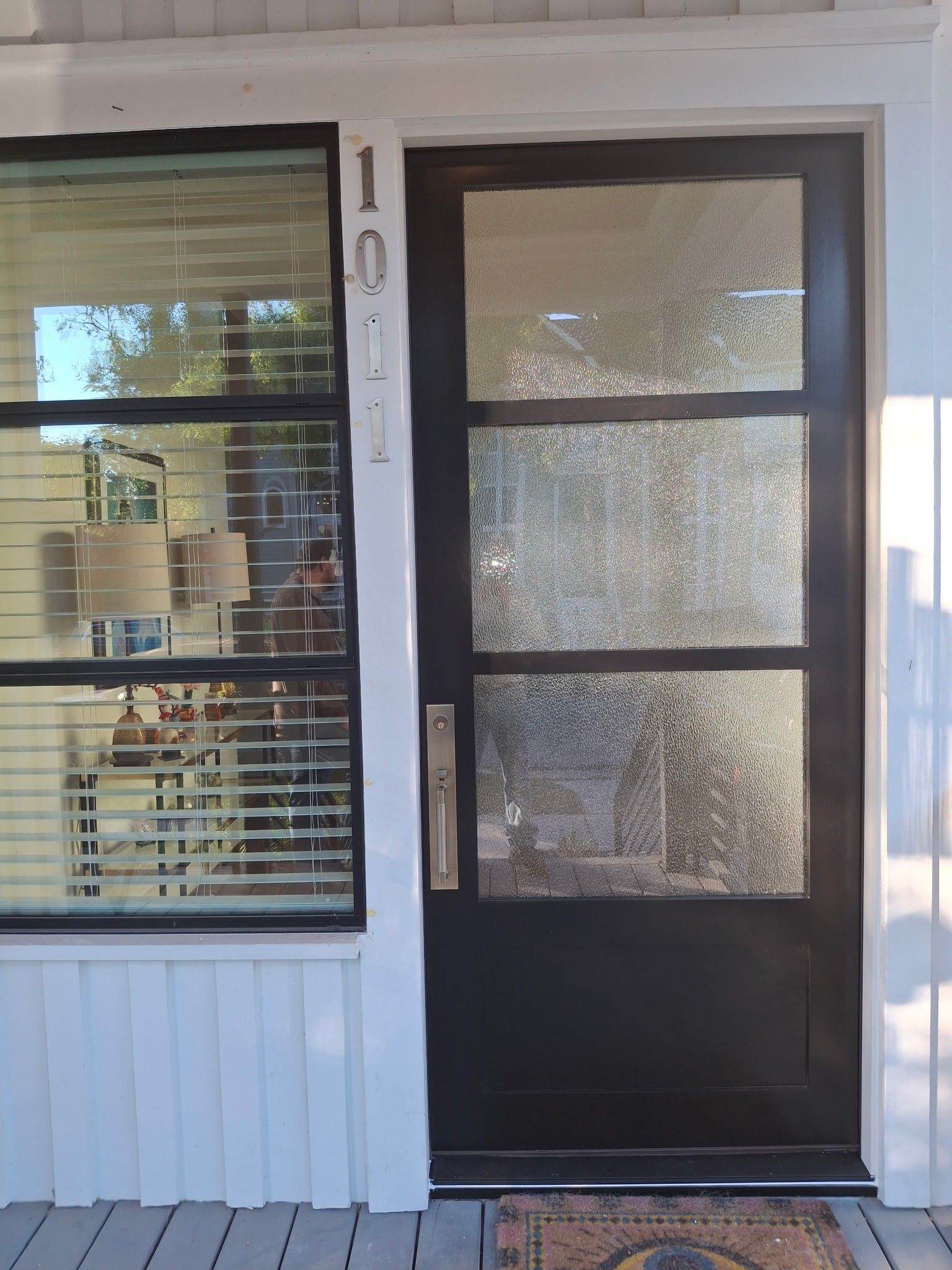 Front porch with a black storm door and window with blinds on a white house exterior.