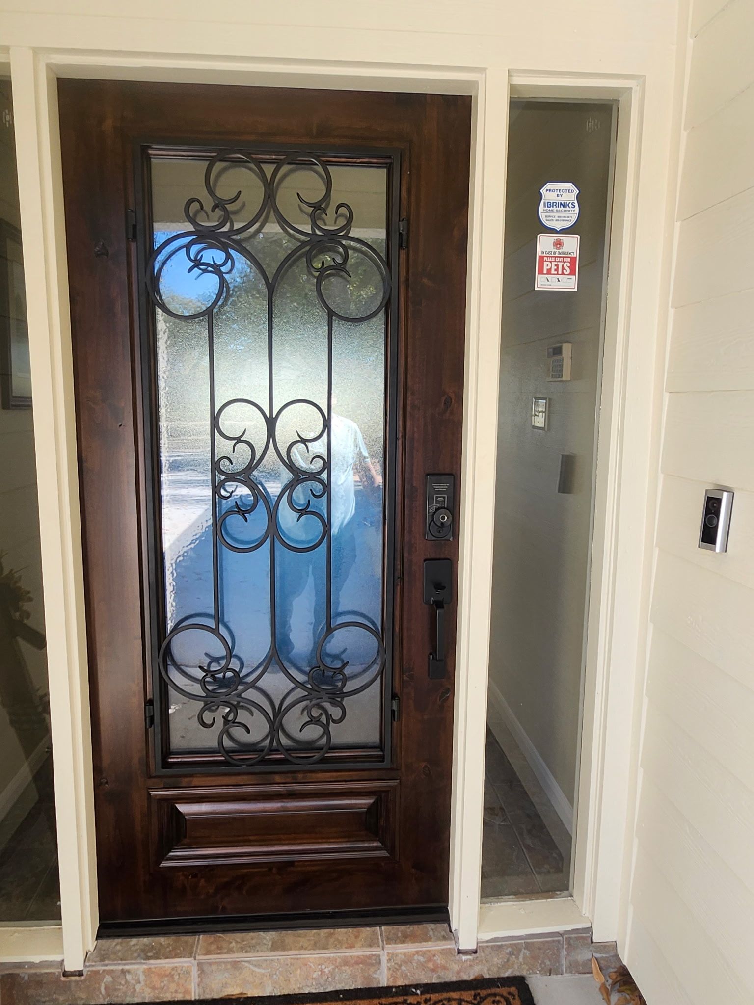 Wooden front door with frosted glass and ornate ironwork in a beige entryway