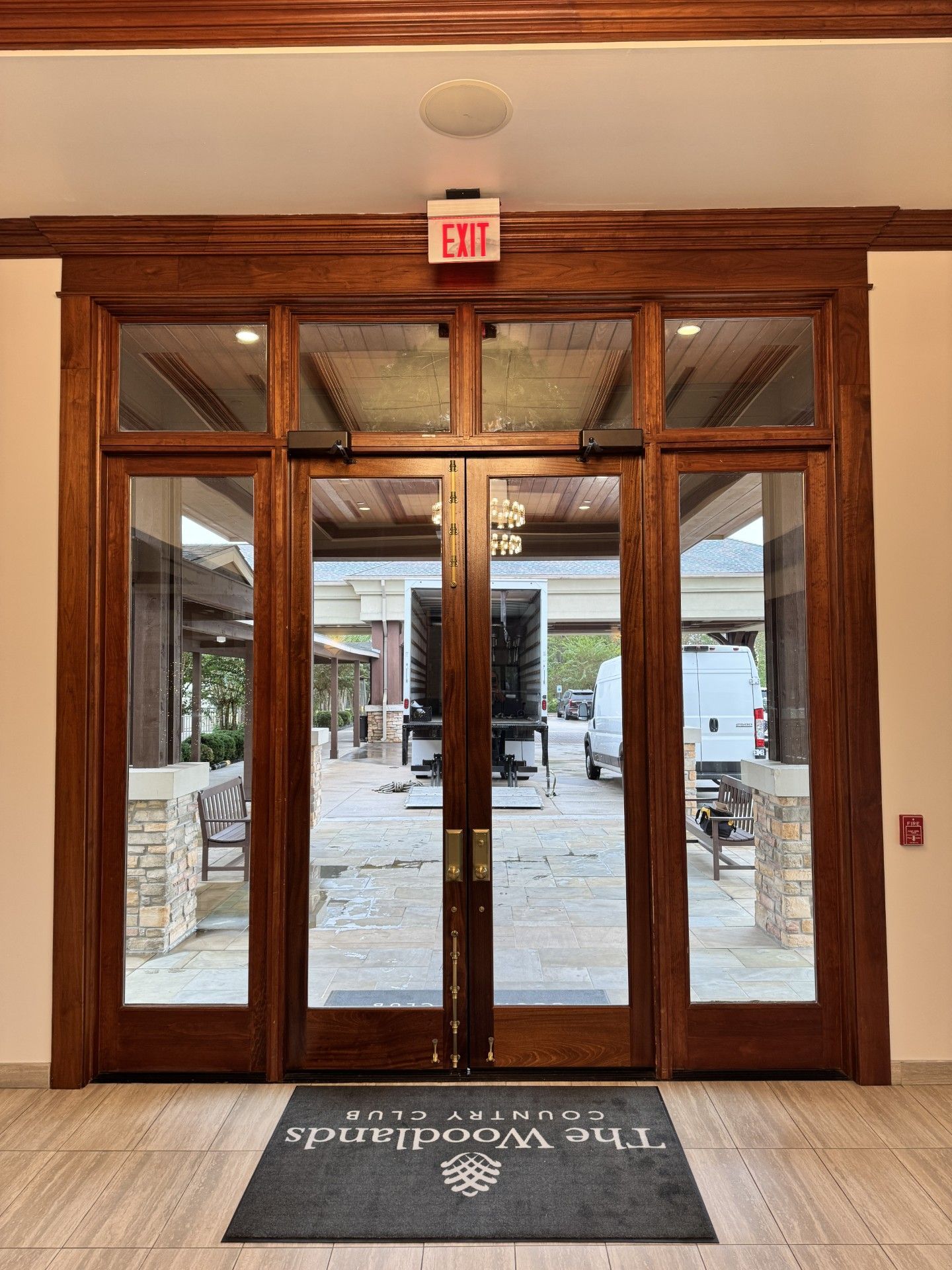 Wooden entry doors with glass panes opening to a snowy outdoor patio, with an EXIT sign above.