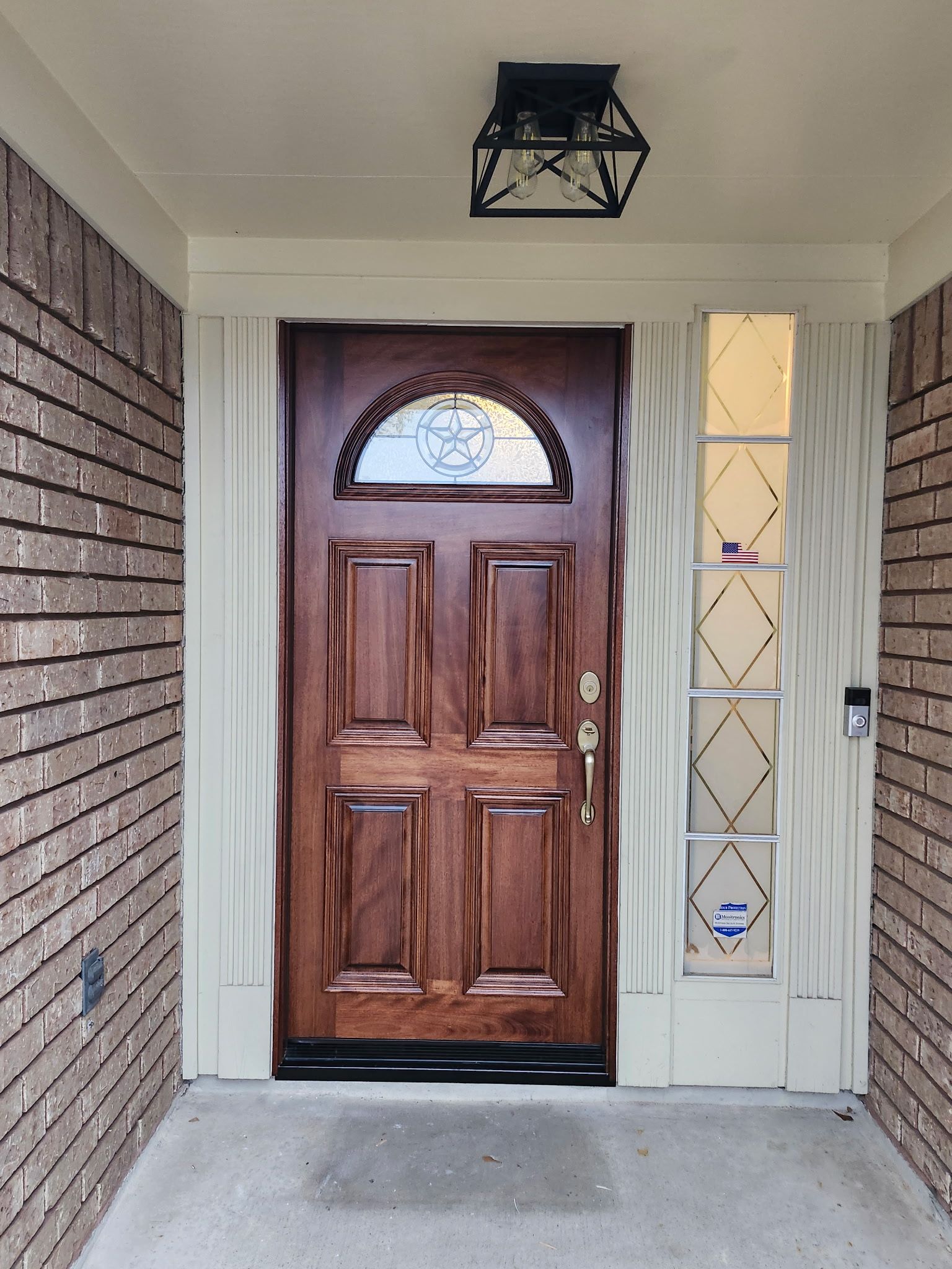 Front porch with a wooden front door, sidelight window, and brick wall under a hanging light.