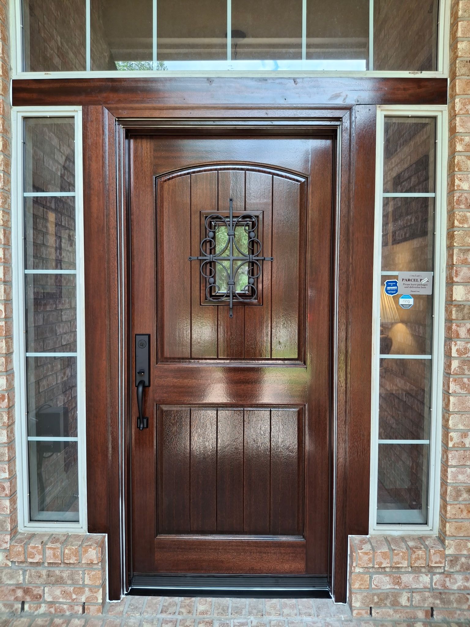 Wooden front door with glass side panels and a small decorative window, set in a brick entryway
