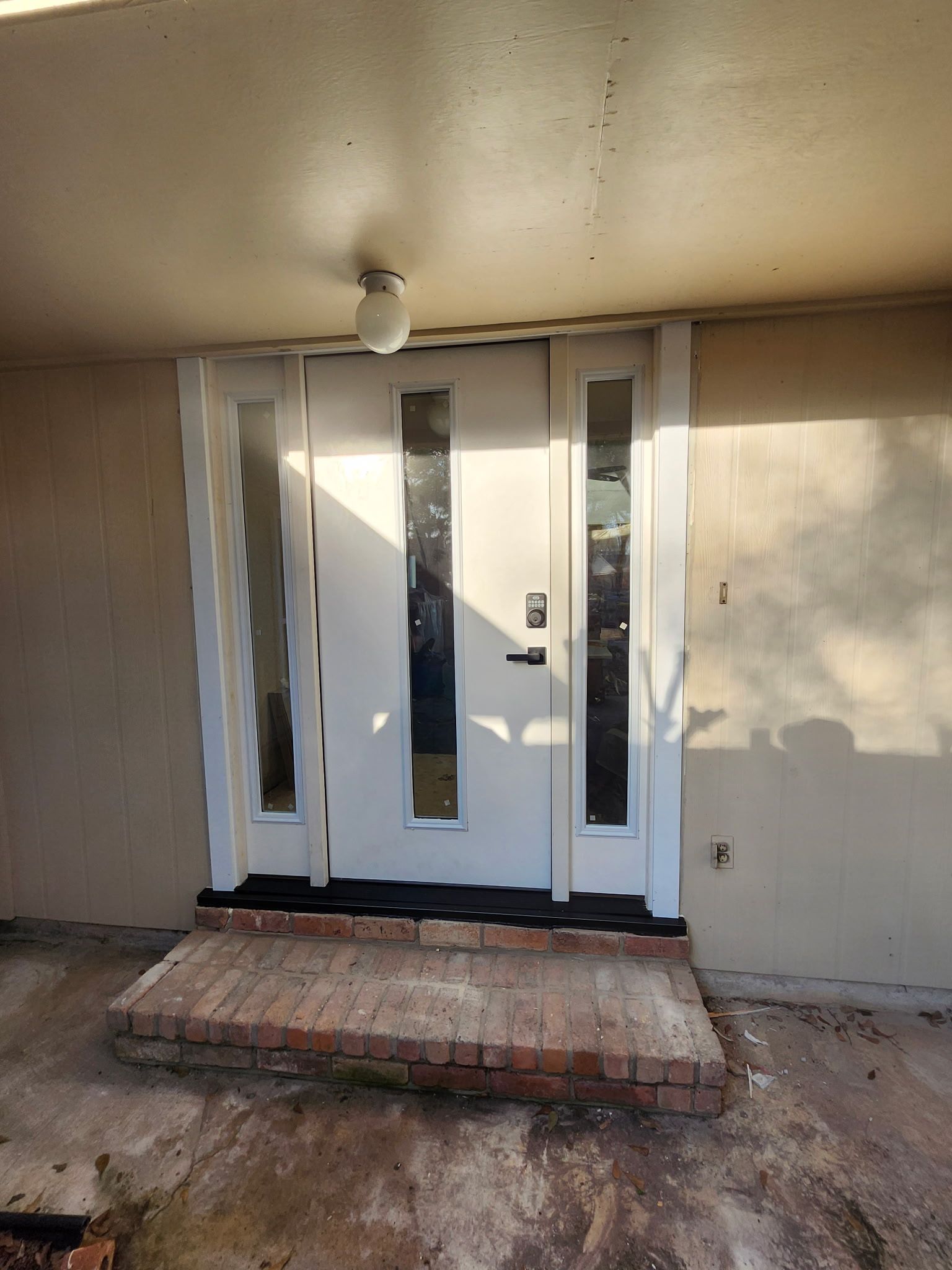 Front entrance with white double doors, brick step, and beige siding under a porch light.