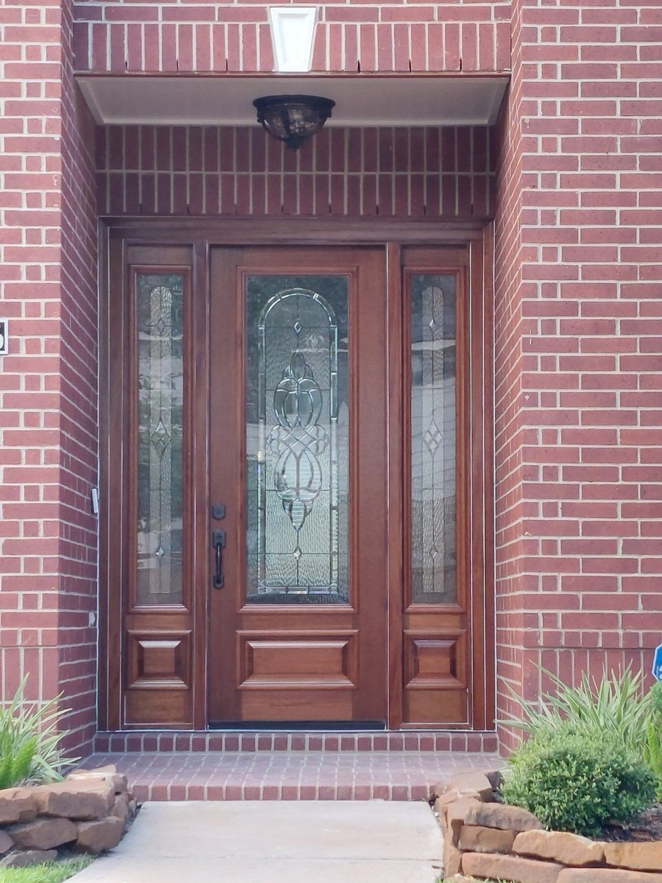 Brick entryway with a wooden front door and decorative glass panels, framed by brick walls and steps.