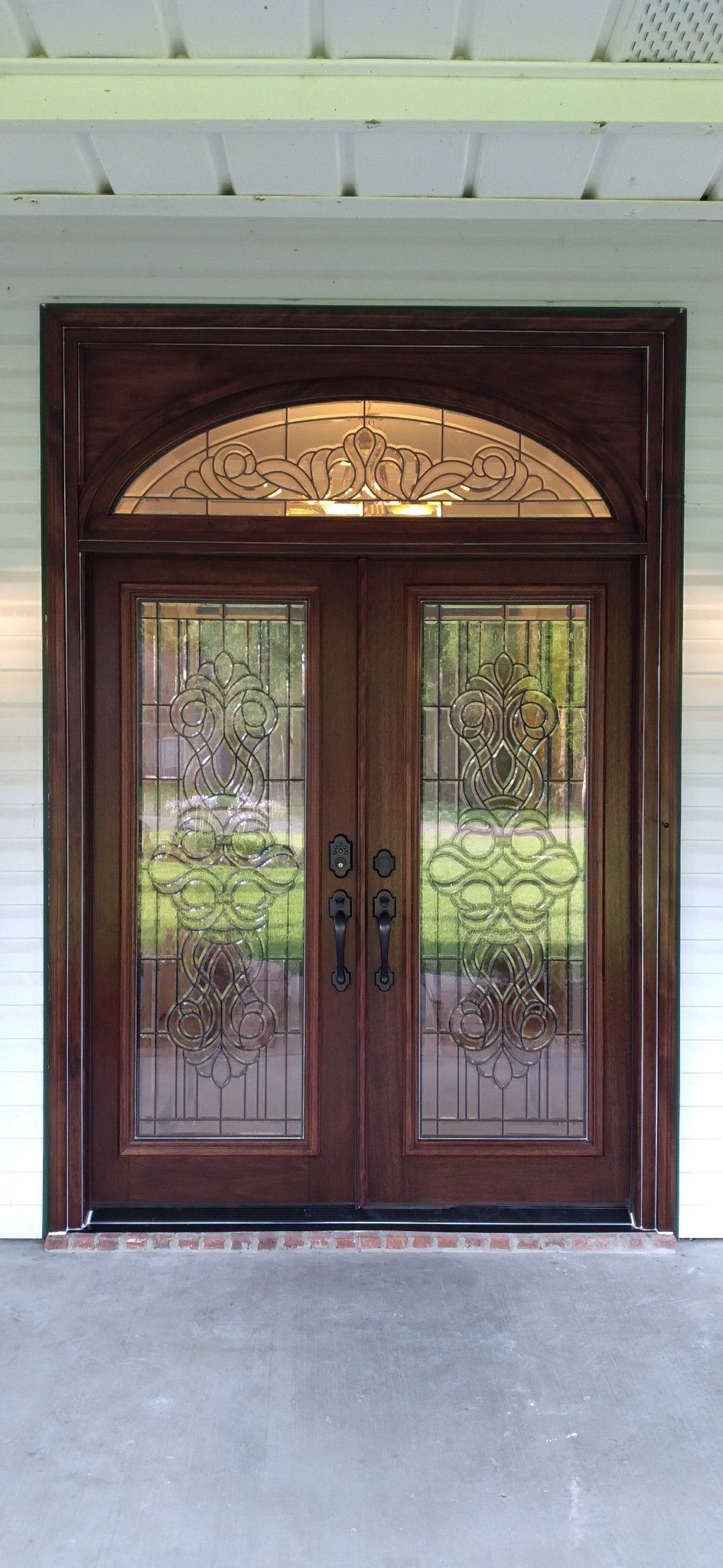 Dark wood double front doors with decorative glass panels and an arched transom under a covered porch.