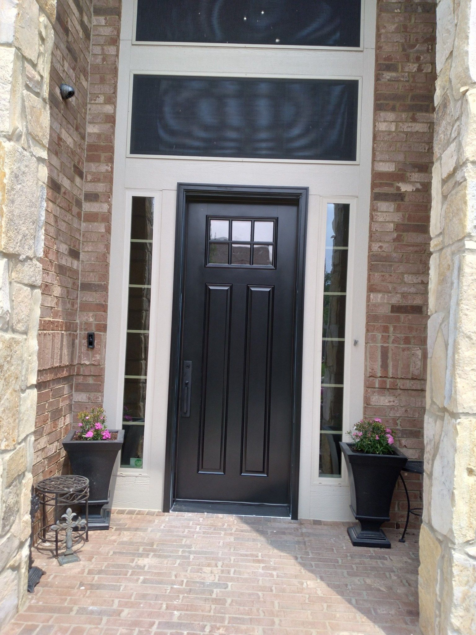 Front door with black door, stone facade, and potted flowers on either side.
