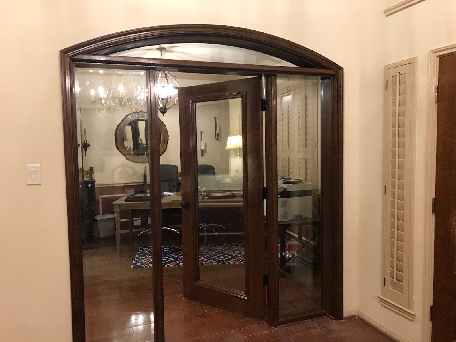 Double wooden doors with glass panels leading into a warmly lit room with a vanity and mirror
