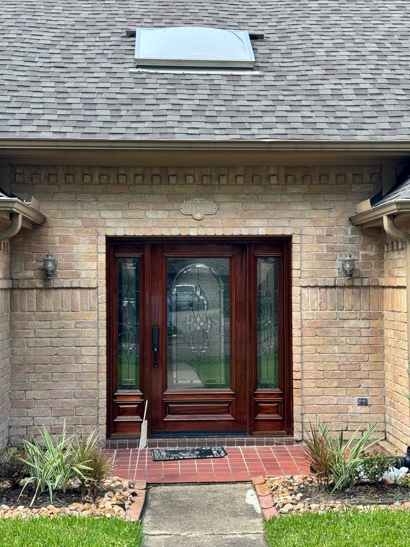 Brick house entrance with double wooden glass doors, small front steps, and a narrow walkway.