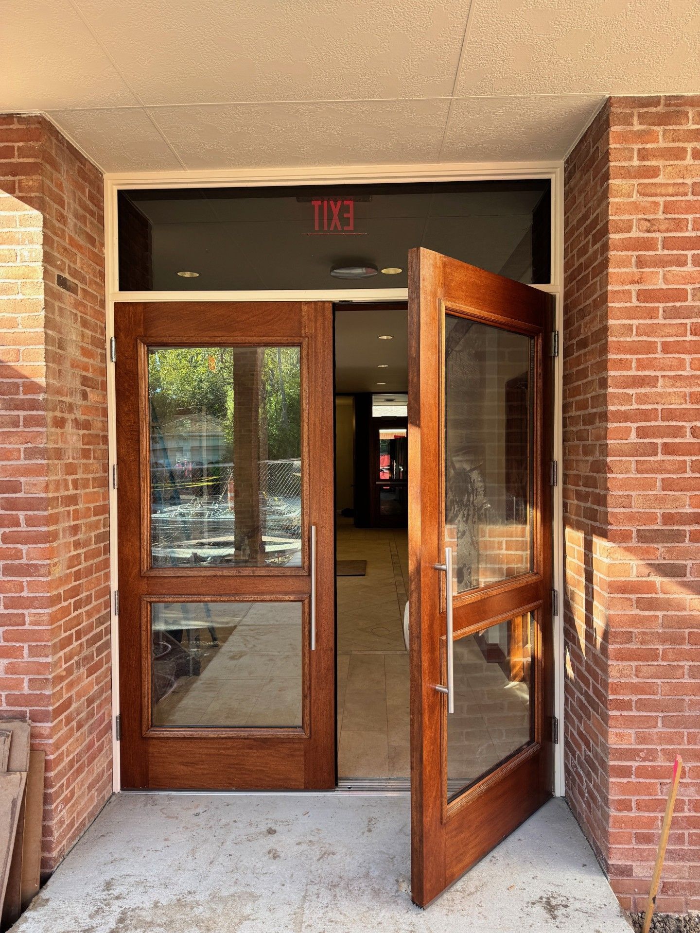 Open brick building entrance with glass double doors, one door propped open, revealing a hallway inside