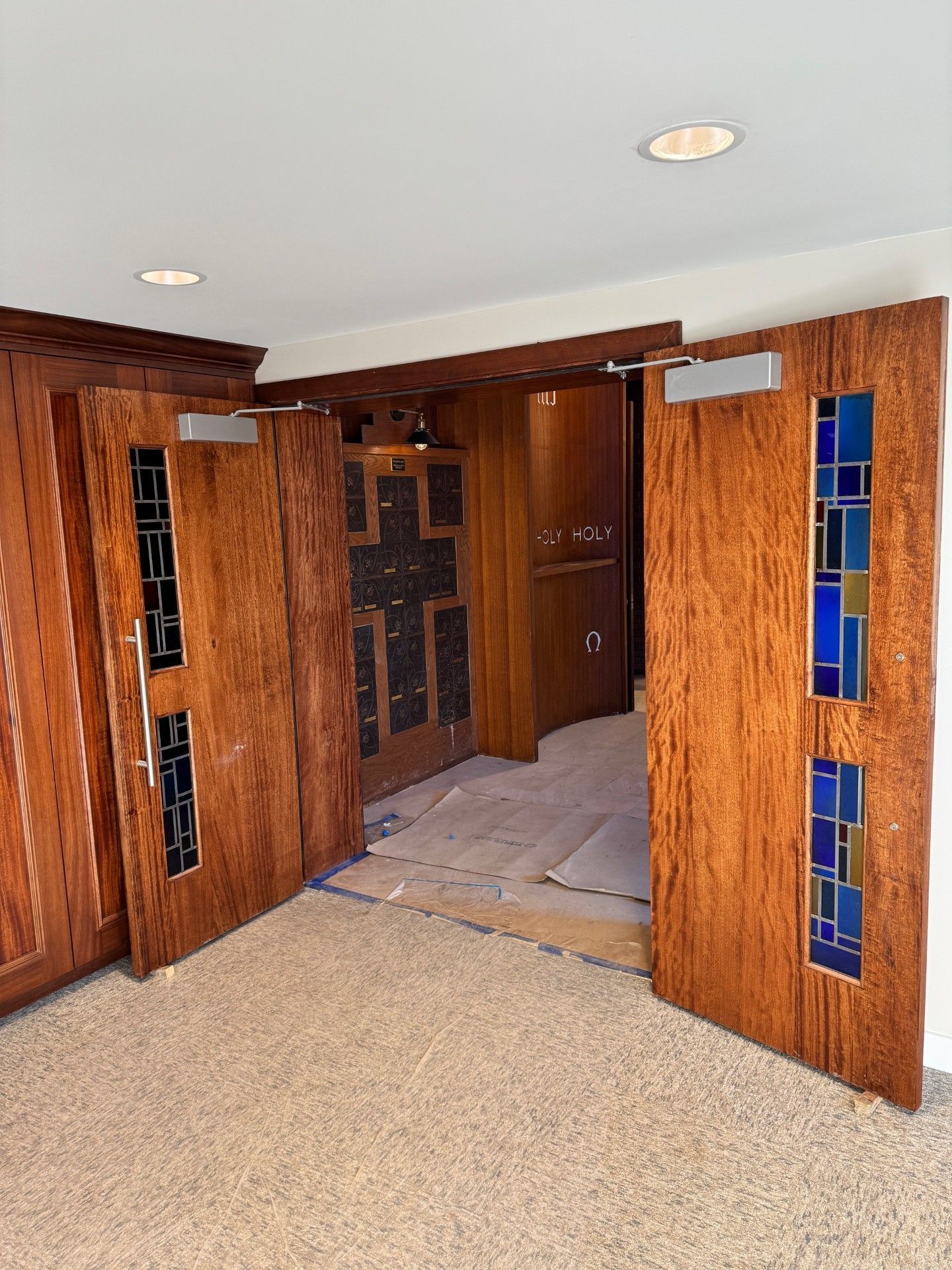 Wood-paneled doorway with open doors, blue glass inserts, and carpeted floor leading into a room