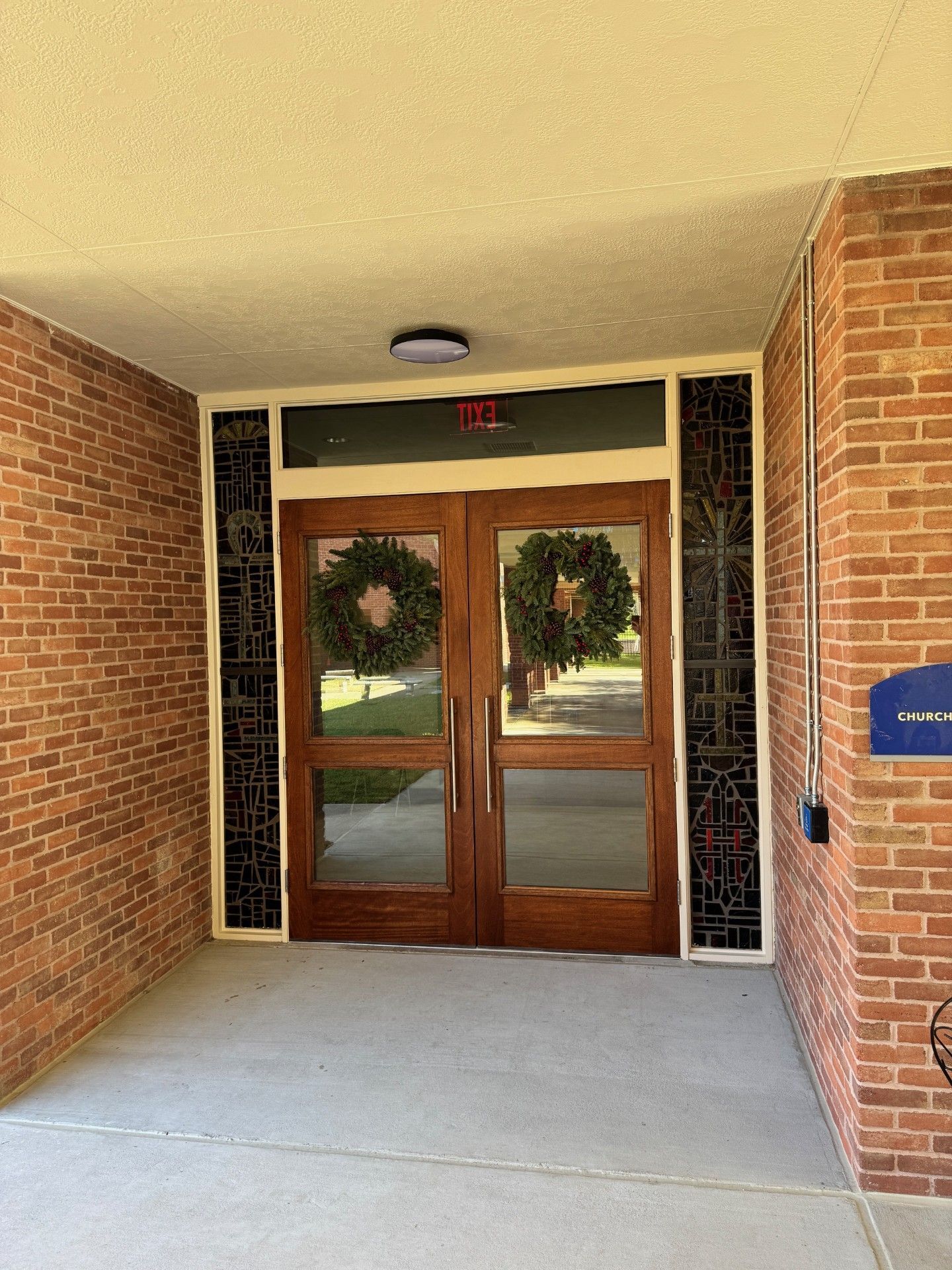 Brick building entrance with wooden double doors, wreaths, and a covered walkway