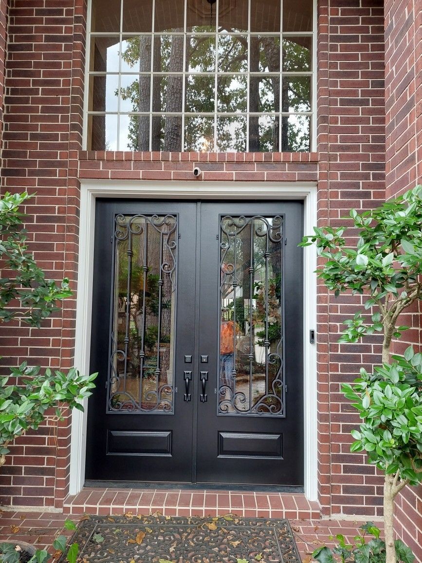Black double front doors in a red brick entryway, framed by windows and green shrubs.