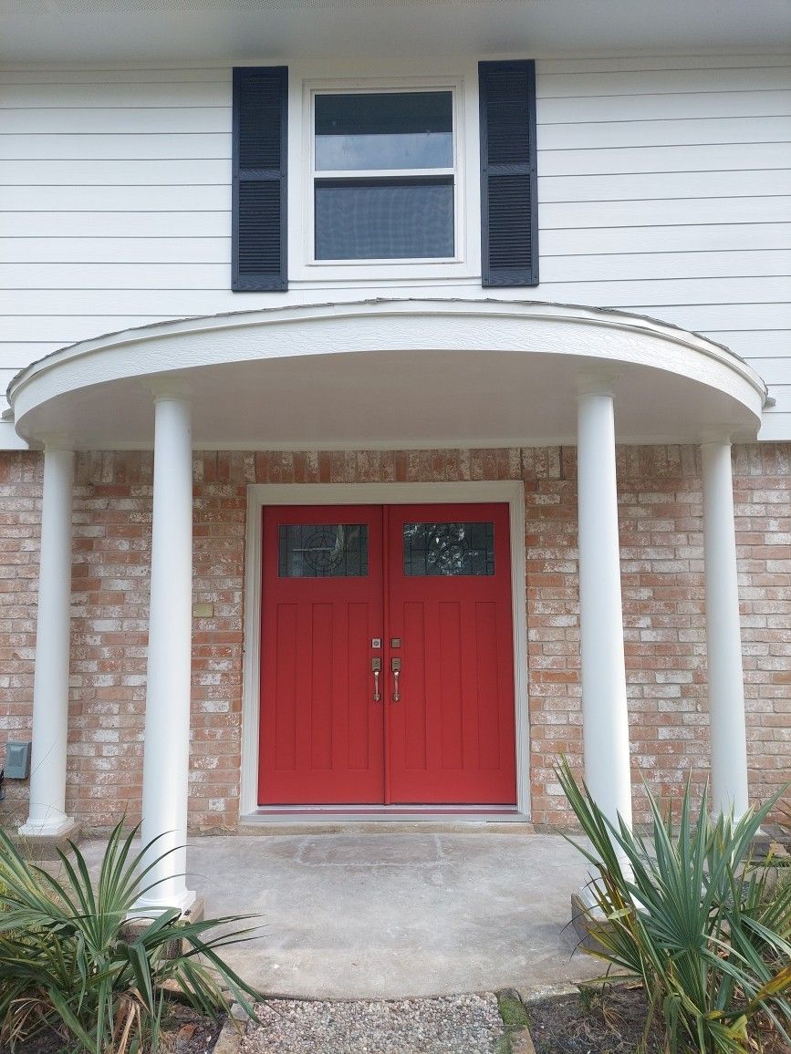 Red double front door under a white porch with columns on a brick house