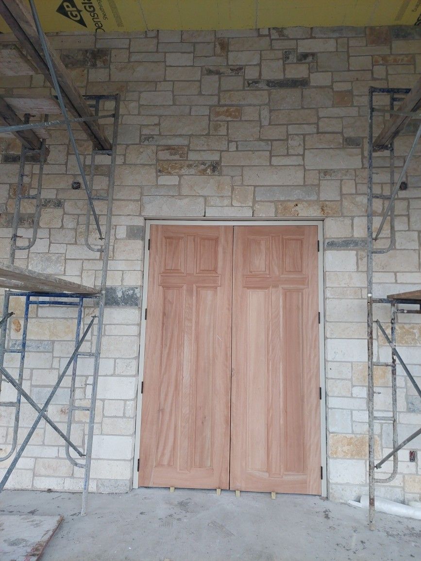 Unfinished stone wall with a wooden double door and metal scaffolding on both sides.